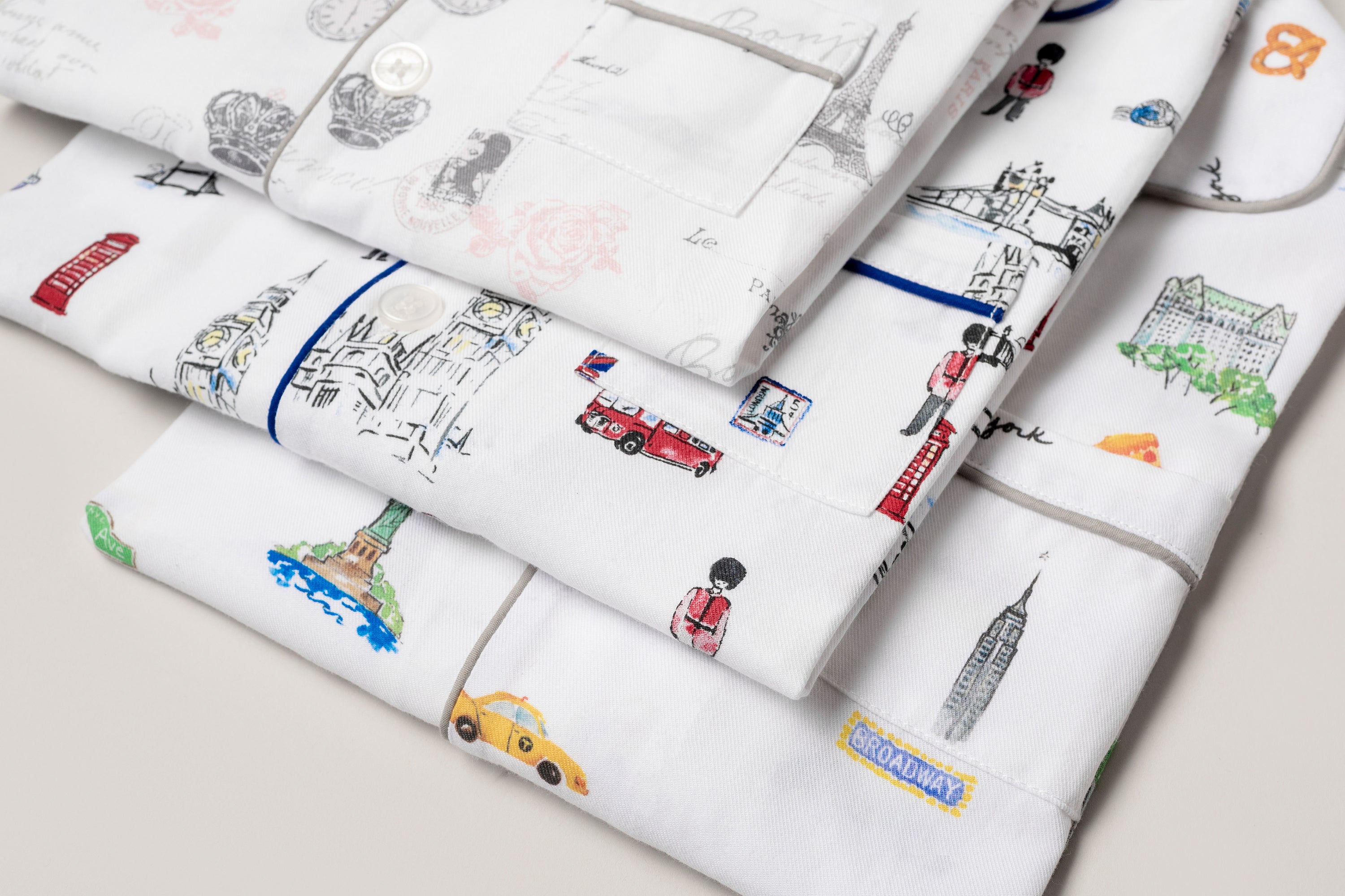 Three folded pieces of white fabric with colorful drawings of famous landmarks, vehicles, and people, including the Statue of Liberty, red buses, and the Empire State Building, on a light background.