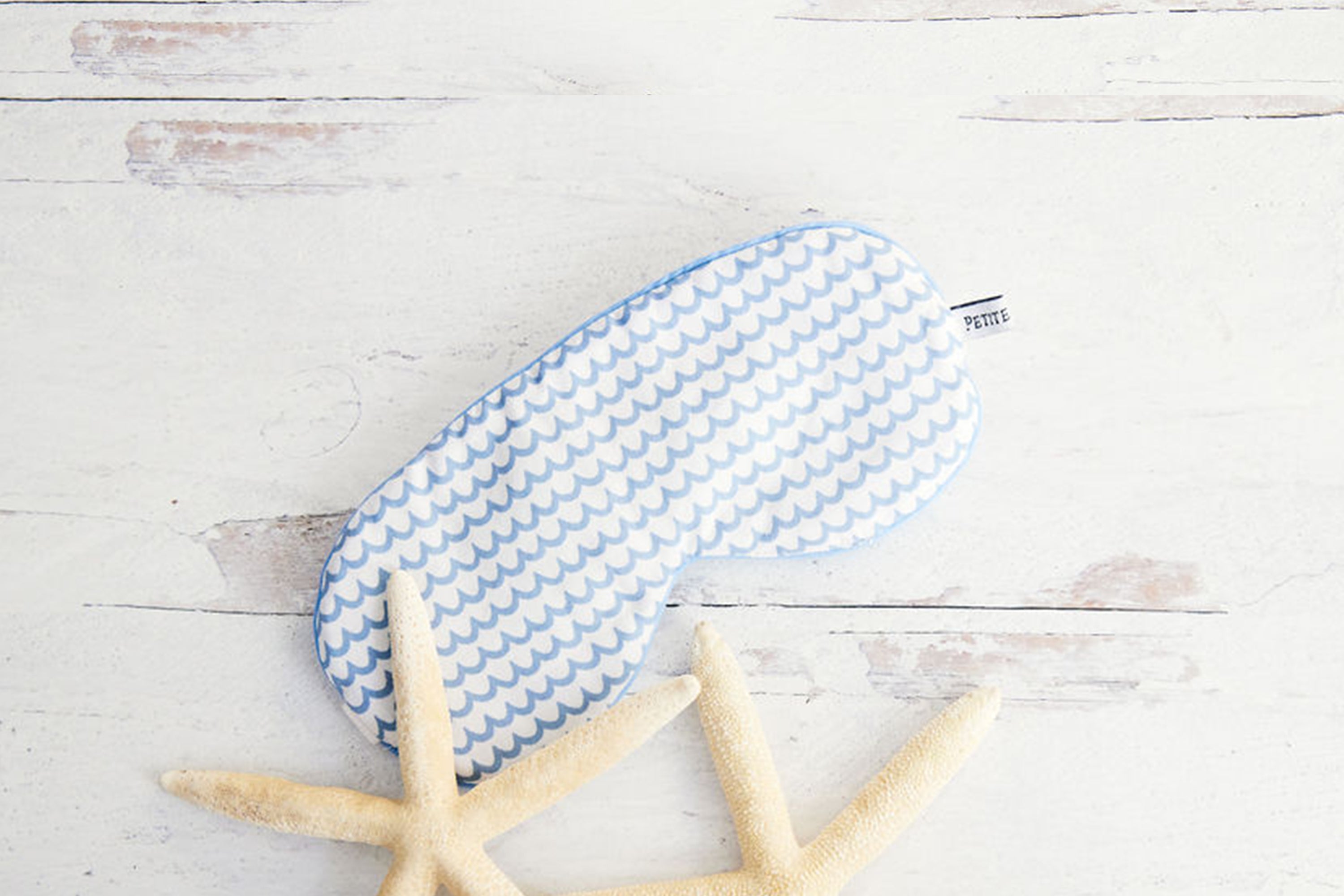 A light blue and white patterned sleep mask rests on a white wooden surface beside two starfish.