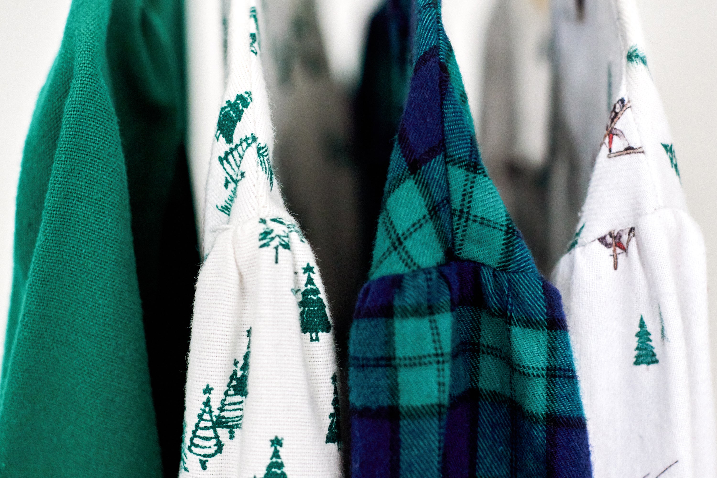 Four hanging clothes: a plain green garment, a white shirt with green Christmas tree prints, a blue and green plaid shirt, and a white shirt with small brown and green skiing illustrations.
