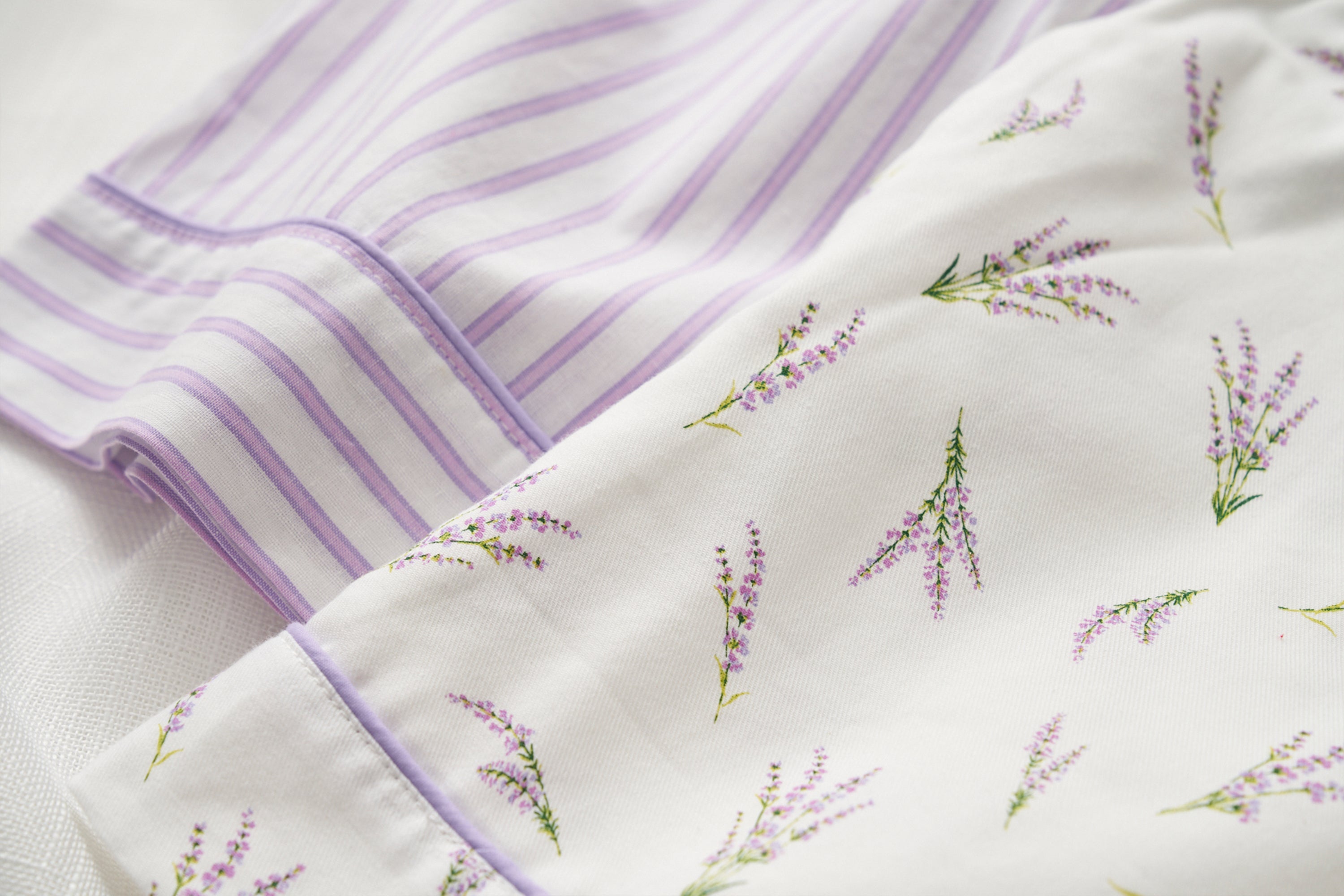 Close-up of textiles featuring lavender designs. One fabric has purple and white stripes, while the other is decorated with small lavender sprigs on a white background.