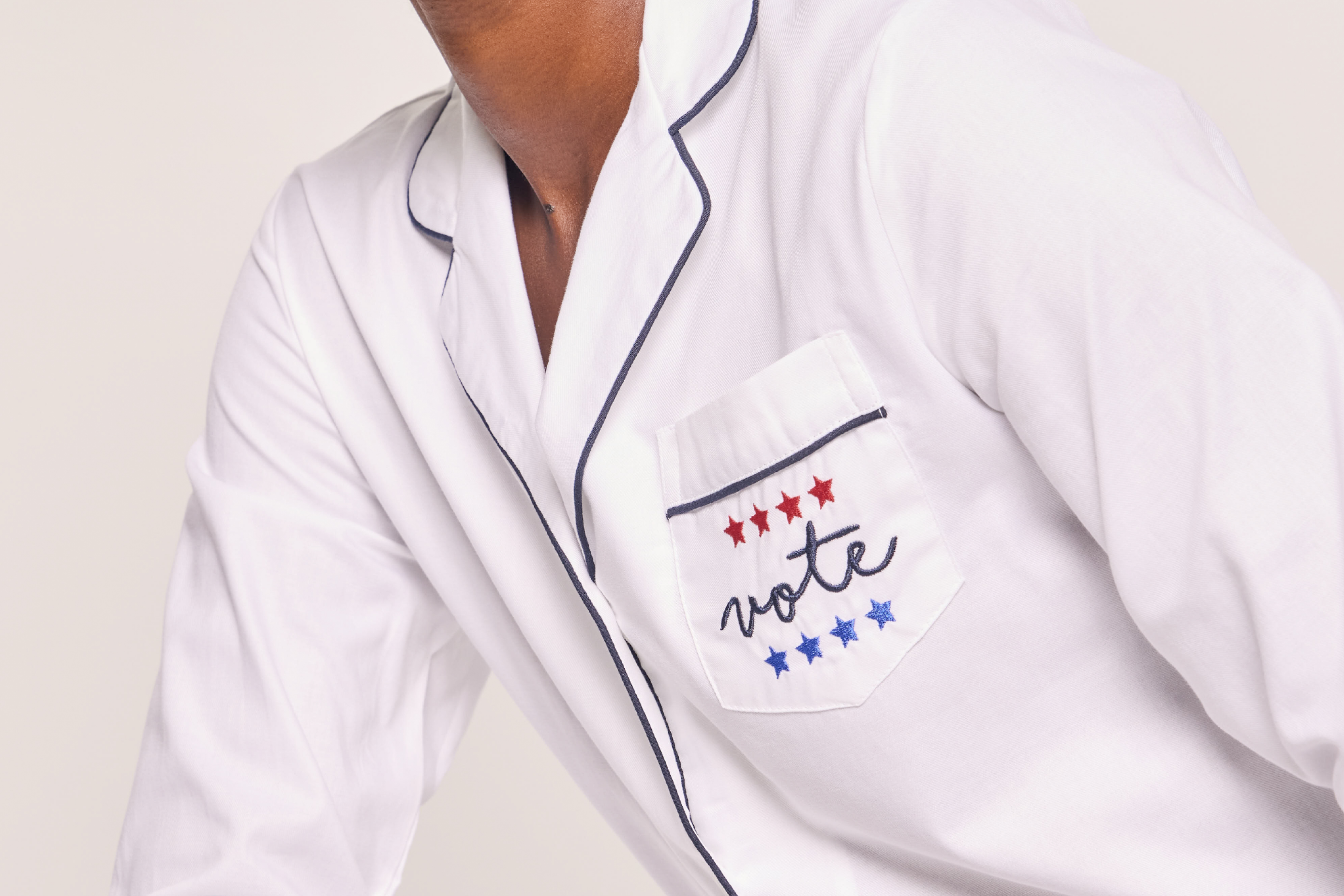 Person wearing white pajamas with black piping; the chest pocket features red and blue stars and the word vote embroidered in cursive. The persons face is not visible.