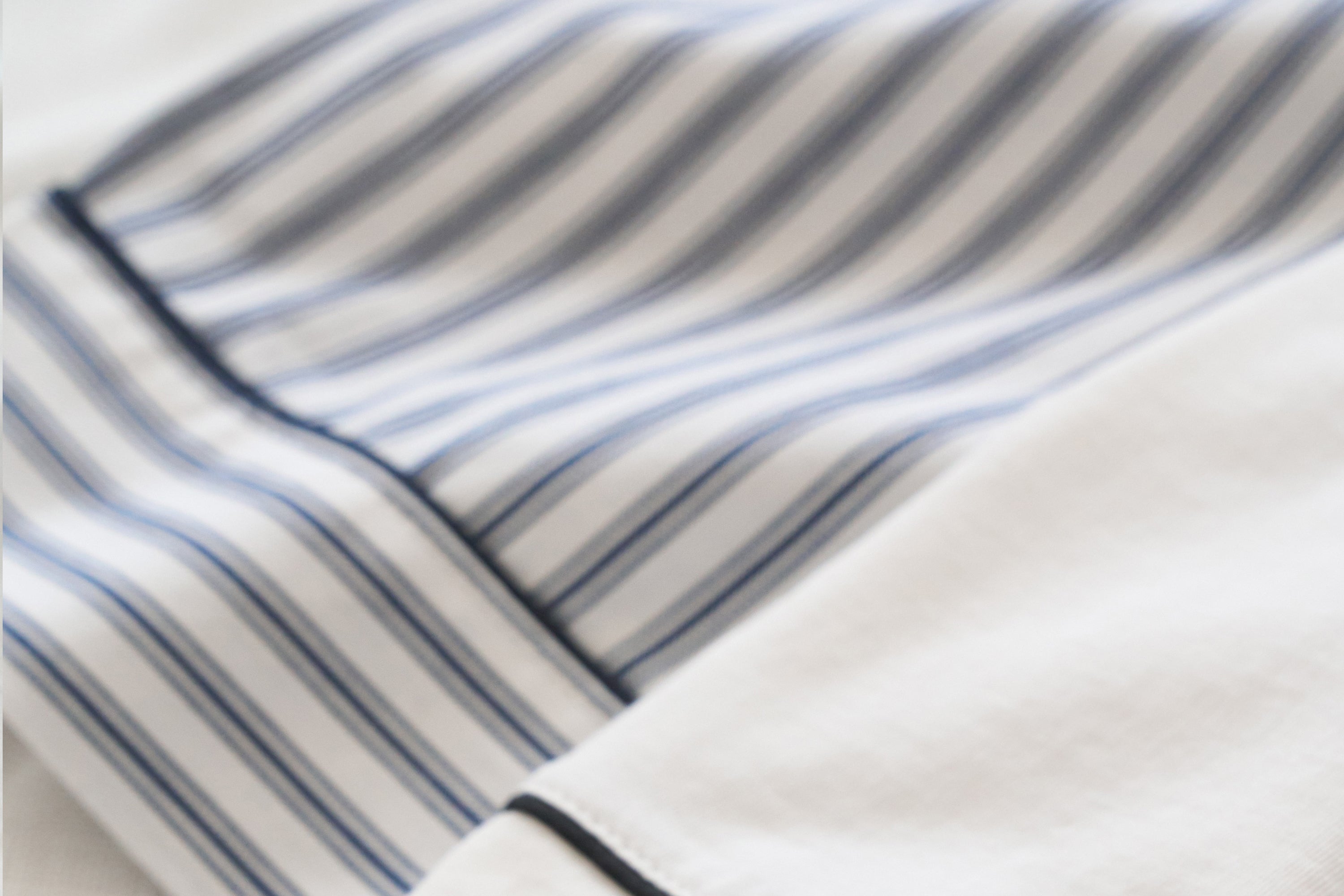 Close-up of a white fabric with blue and gray vertical stripes and a dark seam, possibly part of a shirt or bedding.
