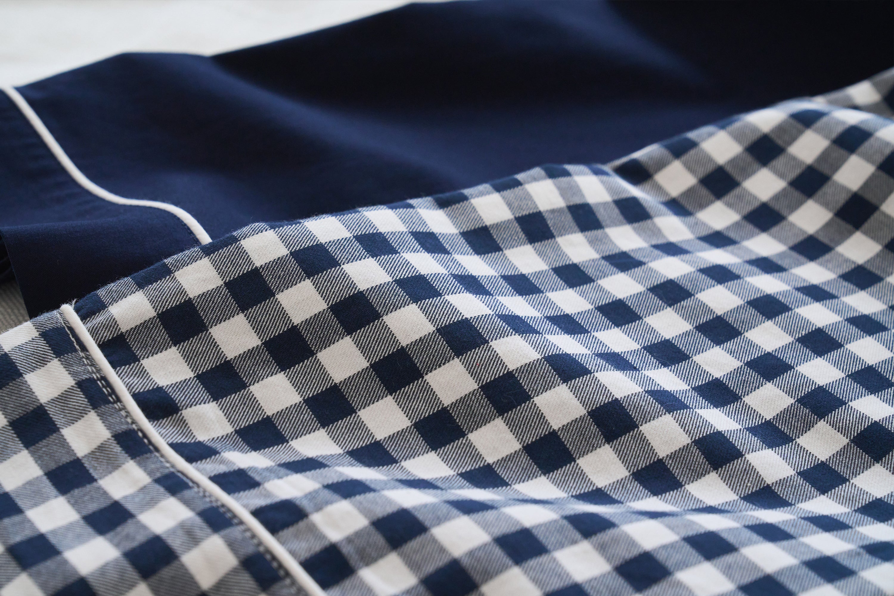 Close-up of fabric with a navy blue and white gingham check pattern next to a solid navy blue section with white piping detail.