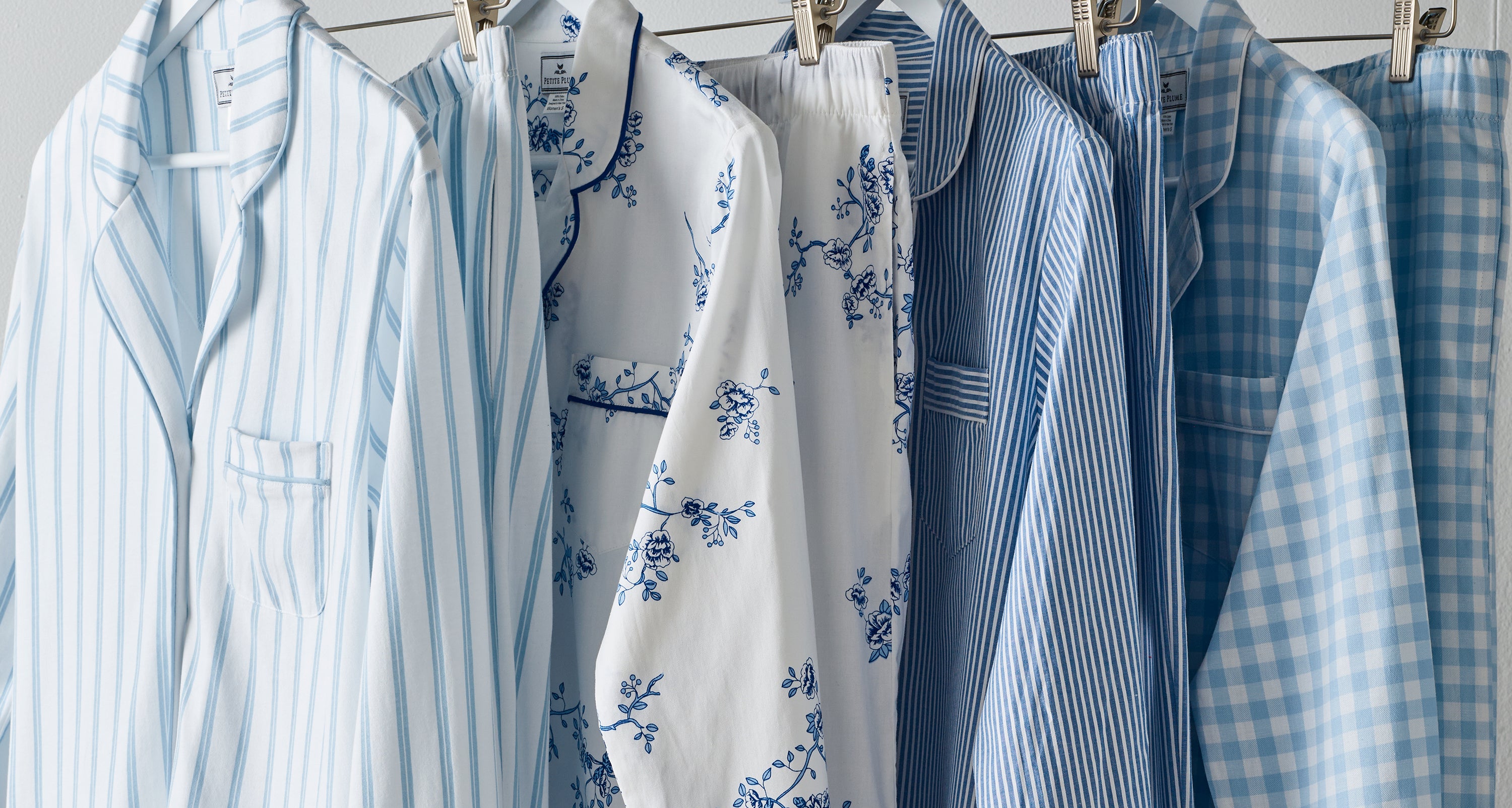 A row of five blue and white patterned pajamas hanging on a rack, featuring stripes, floral, and checkered designs, each with a top and bottom set.