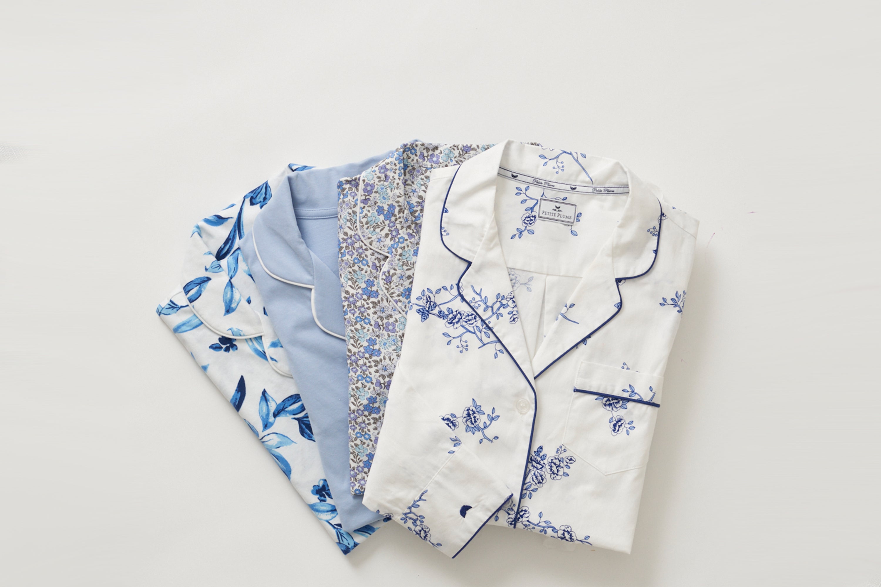 Four folded pajamas with floral and leaf patterns in shades of blue and white, neatly arranged on a light background.