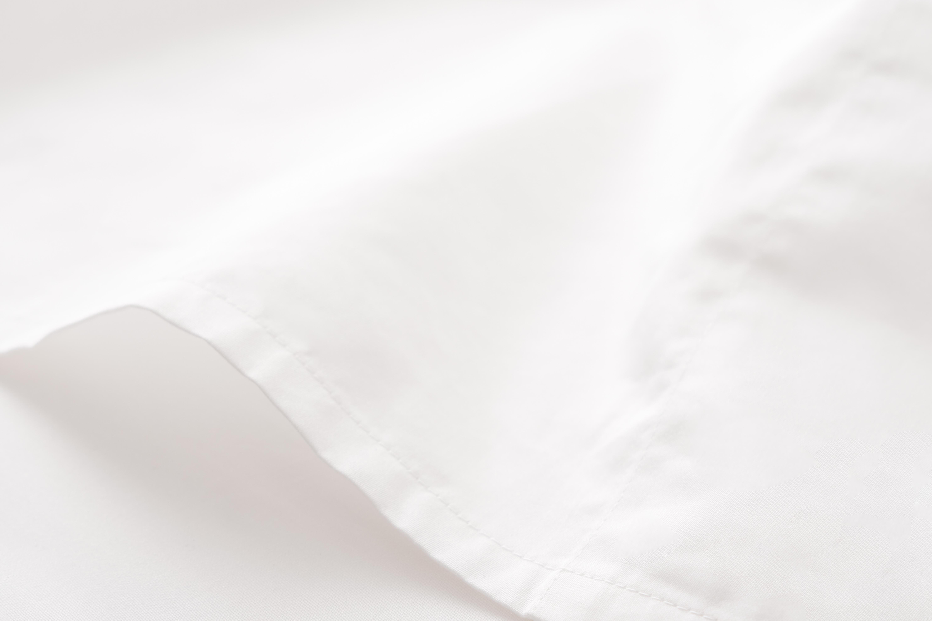 Close-up of a smooth, white fabric with visible stitching, softly lit to highlight its texture and delicate folds.