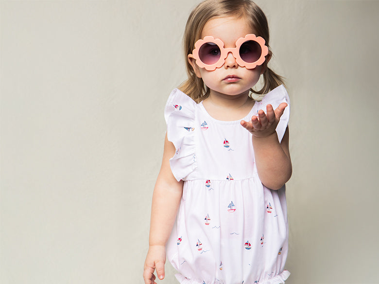 Toddler girl wearing pink flower sunglasses in a White twill romper with a sailboat print