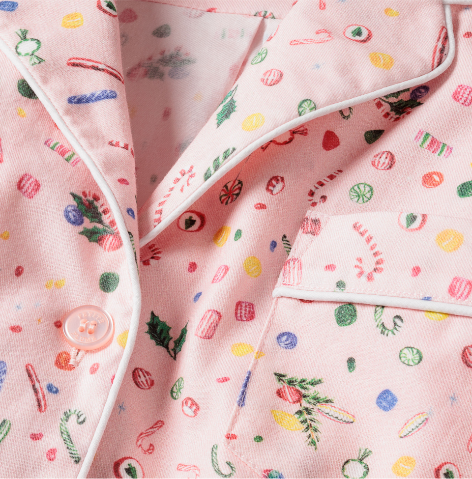 Close-up of pink pajamas with white piping, pink button, and colorful holiday candy and holly leaf pattern, including candy canes, peppermints, and round candies.