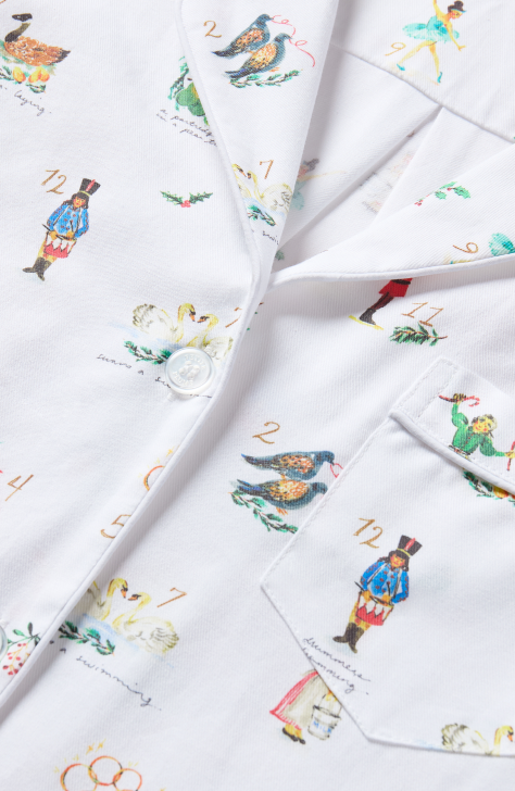 Close-up of a white shirt with colorful illustrations and numbers referencing The Twelve Days of Christmas, featuring characters like a drummer, swans, a goose, and dancers, with white buttons and a front pocket.