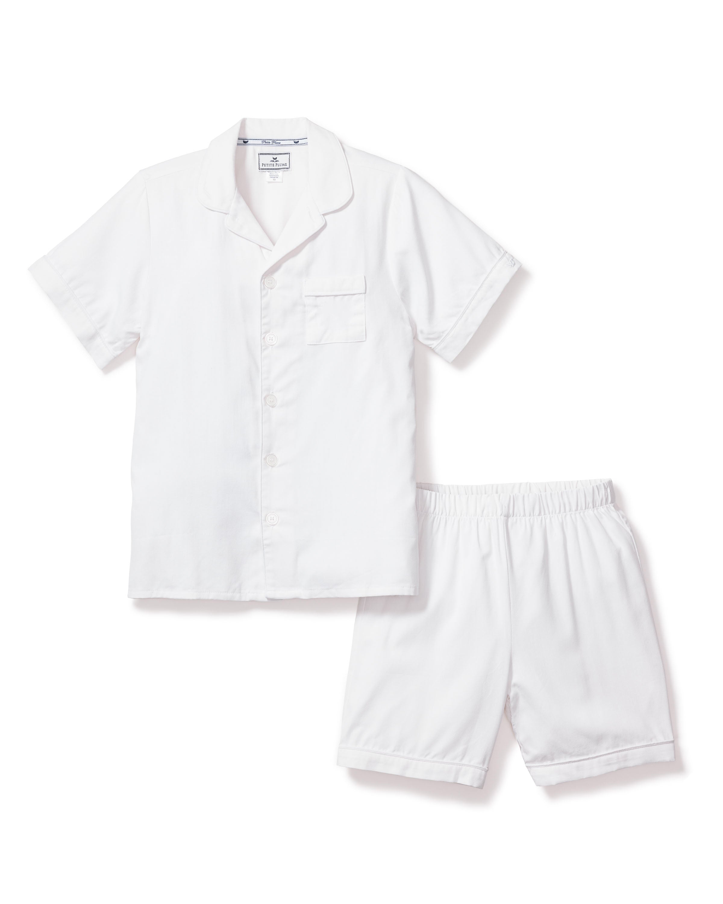 The Kids Twill Pajama Short Set in White by Petite Plume is a neat ensemble made from yarn-dyed cotton, featuring a short-sleeve button-up top with a chest pocket and matching elastic-waist shorts, set against a white background.