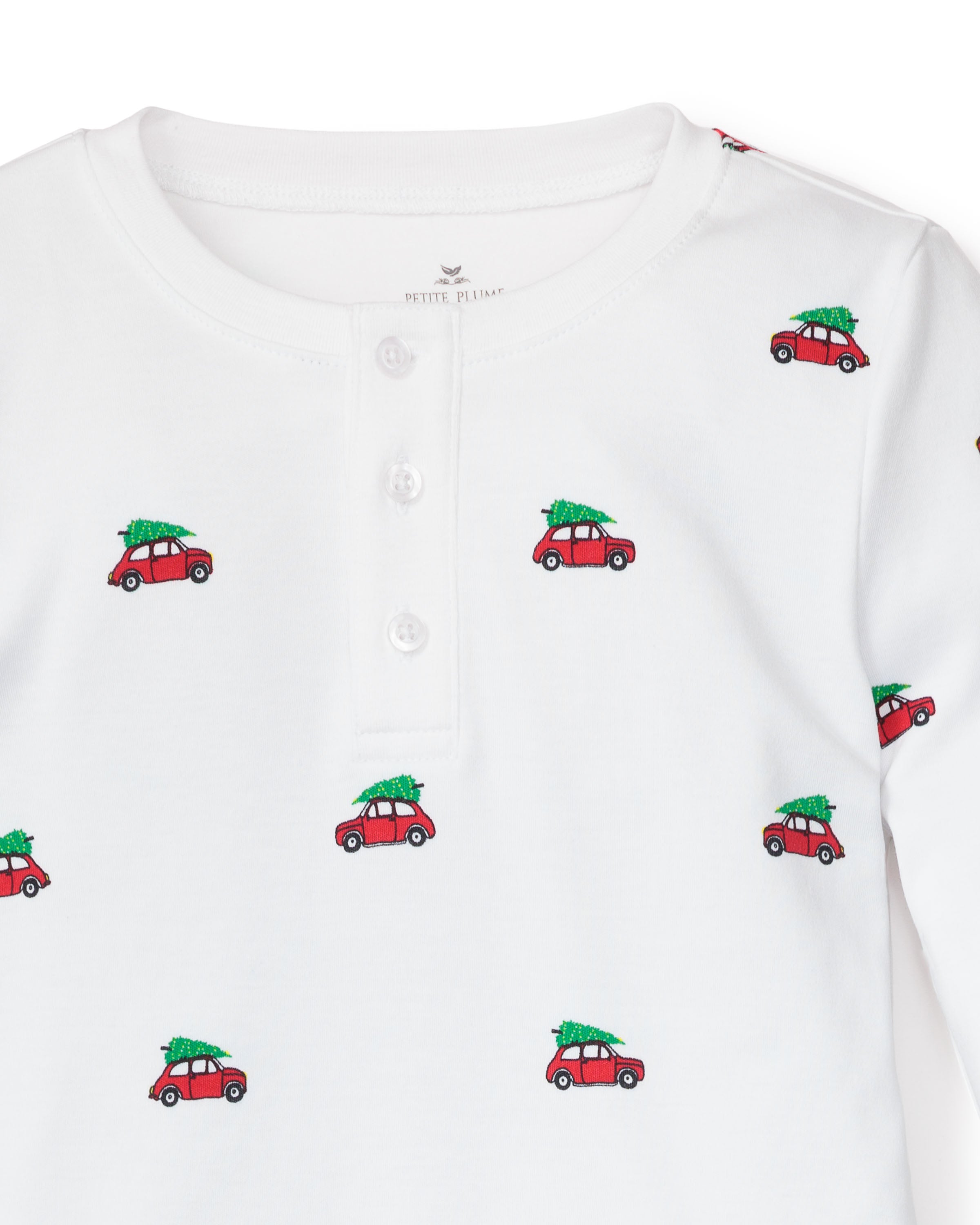 The cozy Kids Pima Snug Fit Pajama Set in Holiday Journey by Petite Plume features a white henley top adorned with small red car prints carrying green Christmas trees, made from soft Pima cotton. It includes a three-button placket and long sleeves for a festive touch.
