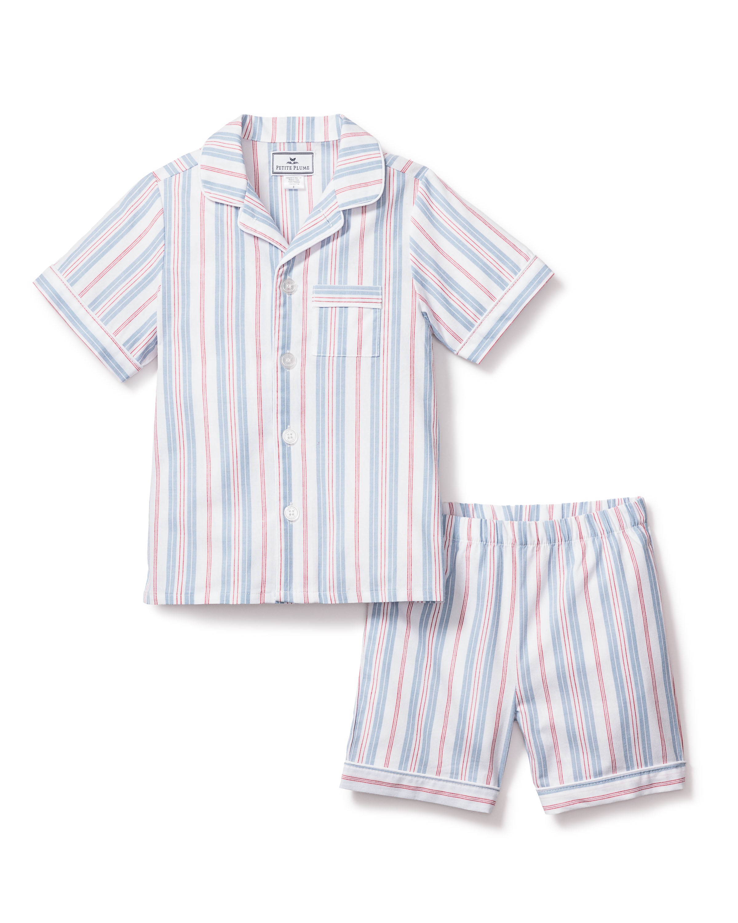 The Kids Twill Pajama Short Set in Vintage French Stripes by Petite Plume features a short-sleeve button-up shirt and shorts in blue, pink, and white vertical stripes. Complete with a stylish chest pocket and collar, this set offers both charm and comfort.