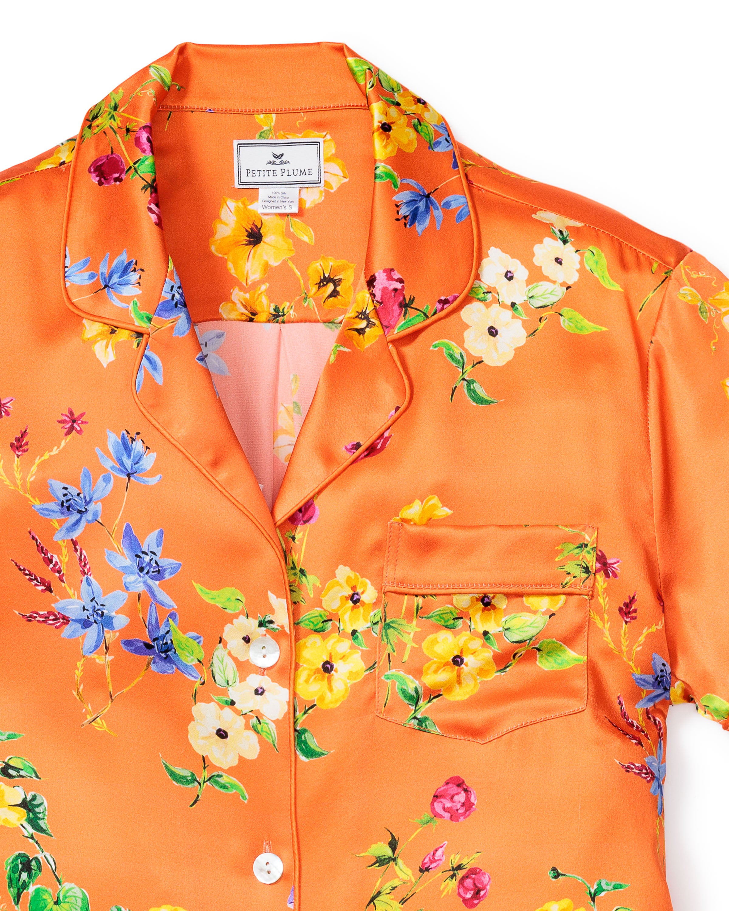 Petite Plumes Womens Silk Pajama Set in Tangerine Brilliant Botanical features a luxurious top with blue, white, and yellow floral prints, a collar, front pocket, and elegant white buttons.