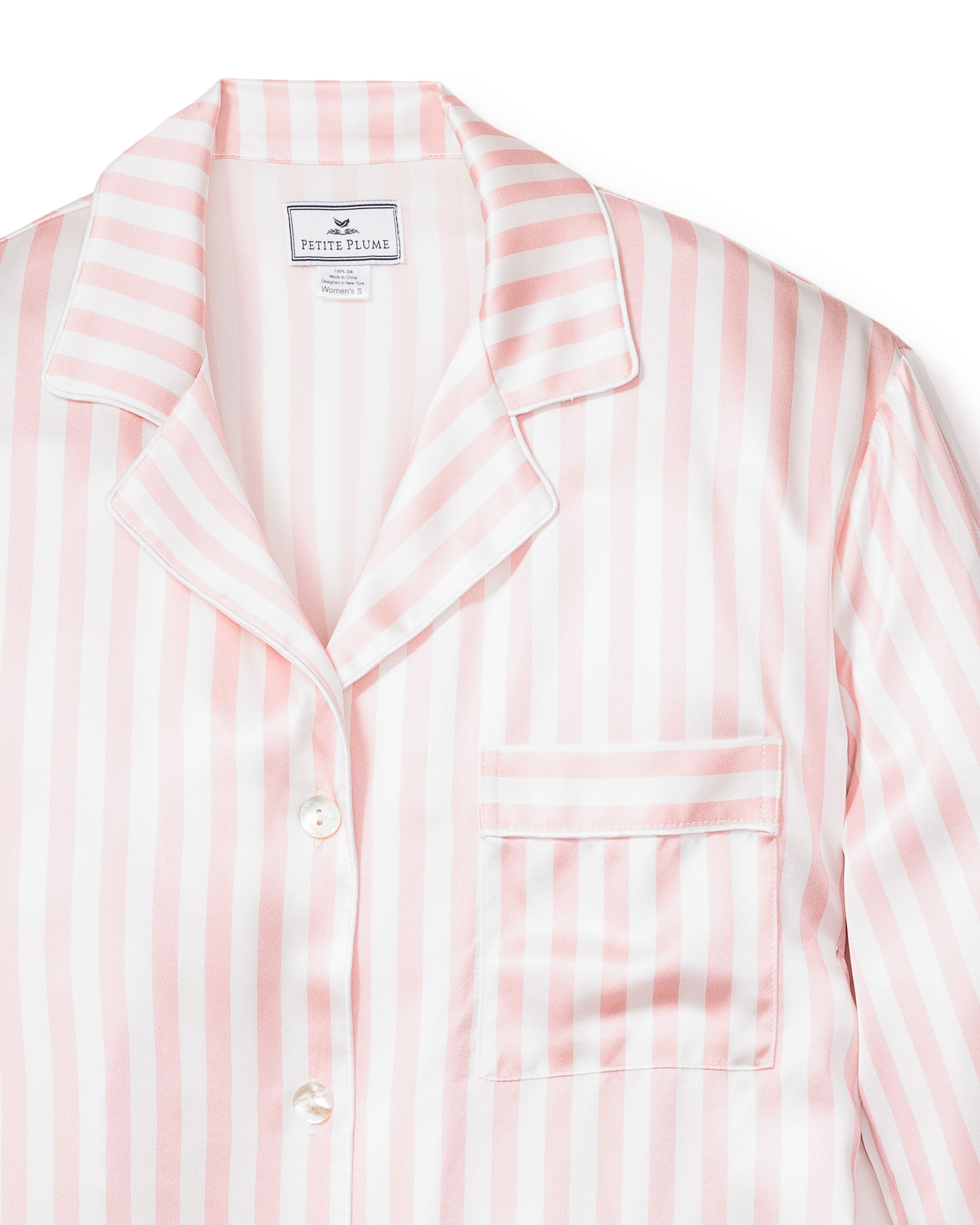The Womens Silk Pajama Set in Pink Stripe by Petite Plume features a luxurious top with a lapel collar, chest pocket, and elegant white buttons. Its silky fabric combines comfort and style, perfect for any luxury sleepwear collection.