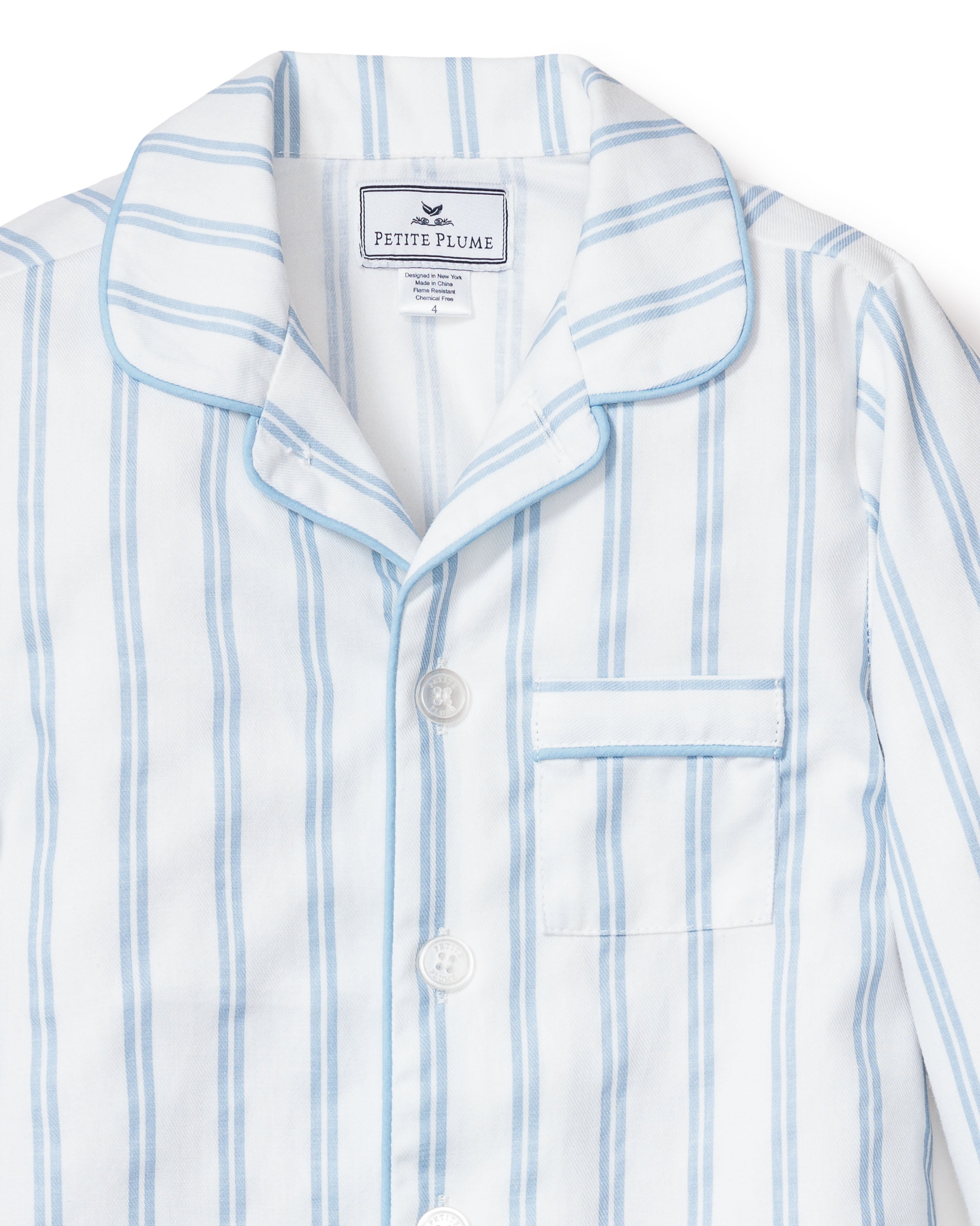 The Kids Twill Pajama Set in Periwinkle and White Stripe by Petite Plume features soft yarn-dyed cotton, classic collar, white buttons, a front pocket with a branded tag, and blue piping for timeless comfort.