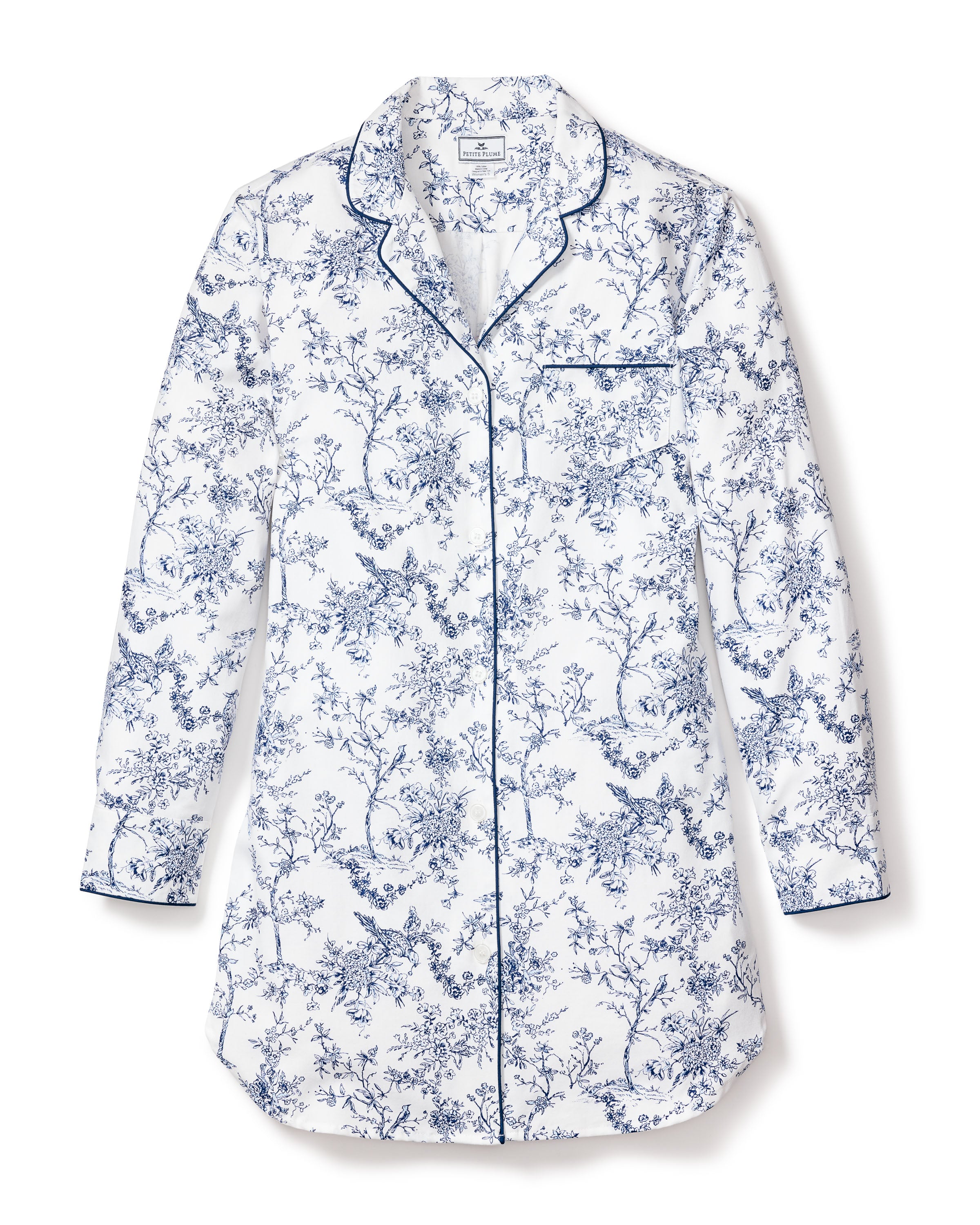 The Womens Twill Nightshirt in Timeless Toile by Petite Plume is a luxurious white long-sleeved shirt with a blue floral pattern and dark piping. Made from the finest quality cotton, it features a chest pocket and button-up front, embodying refined elegance.