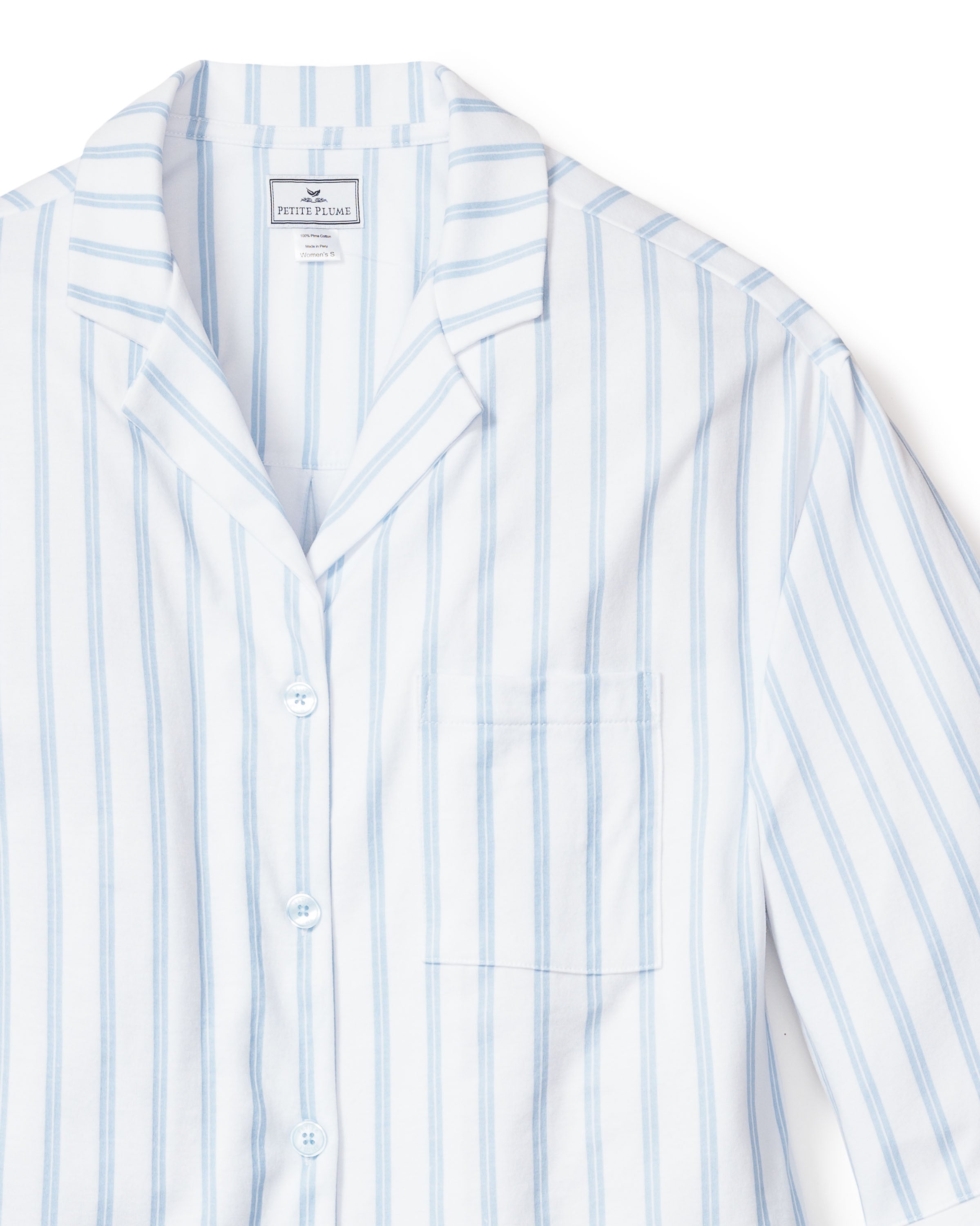 A close-up of Petite Plumes The Olivia Wide Leg Pima Pajama Set in Periwinkle Stripe, featuring a white button-up shirt with light blue vertical stripes. Crafted from breathable fabric, it includes a chest pocket and neat collar, embodying the luxurious feel of Pima cotton sleepwear.