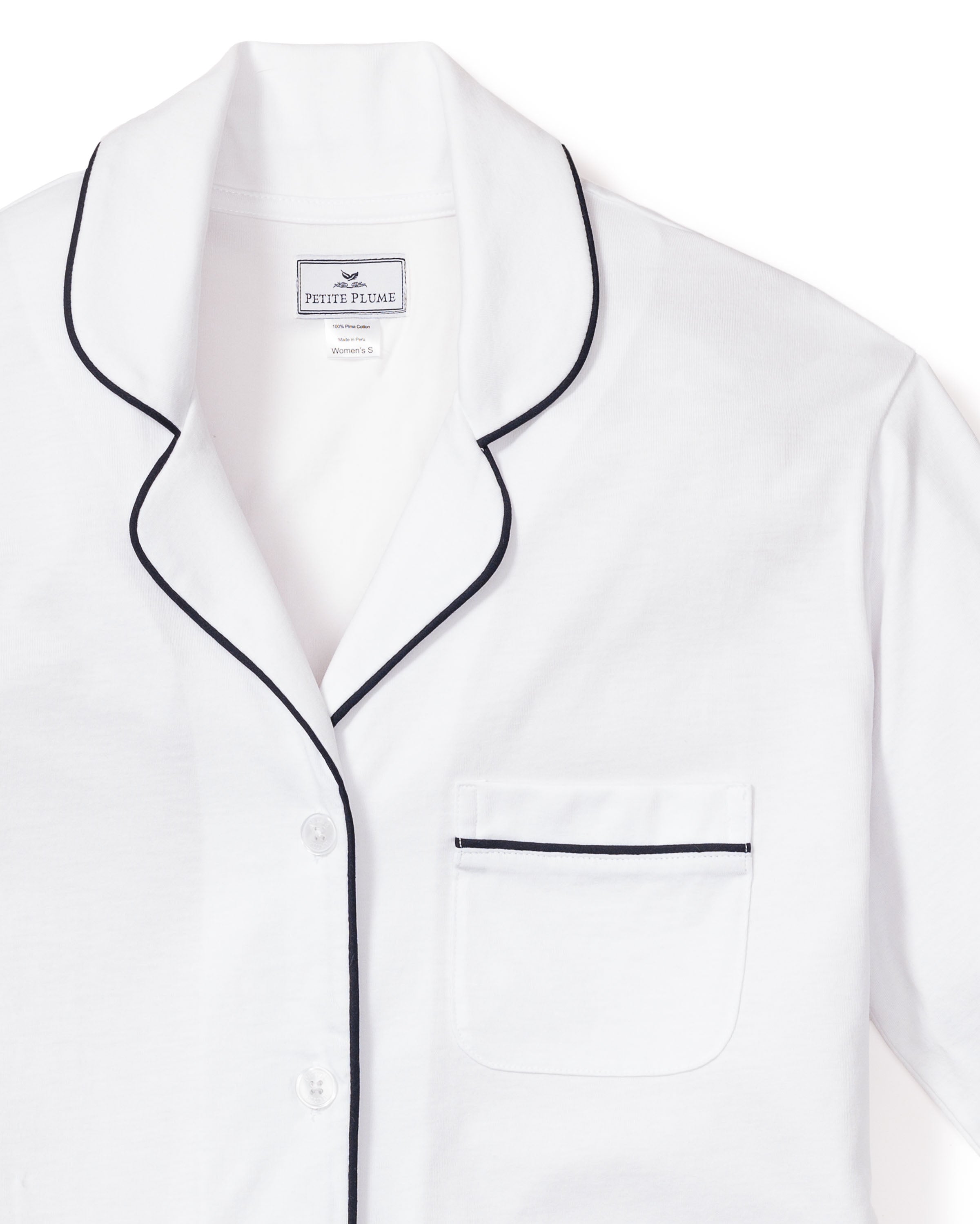 The Womens Pima Long Sleeve Short Set by Petite Plume features a white collared pajama top with navy piping on the collar, pocket, and edges. This luxurious sleepwear includes a button-up shirt and chest pocket accented with navy trim in classic PJ style.
