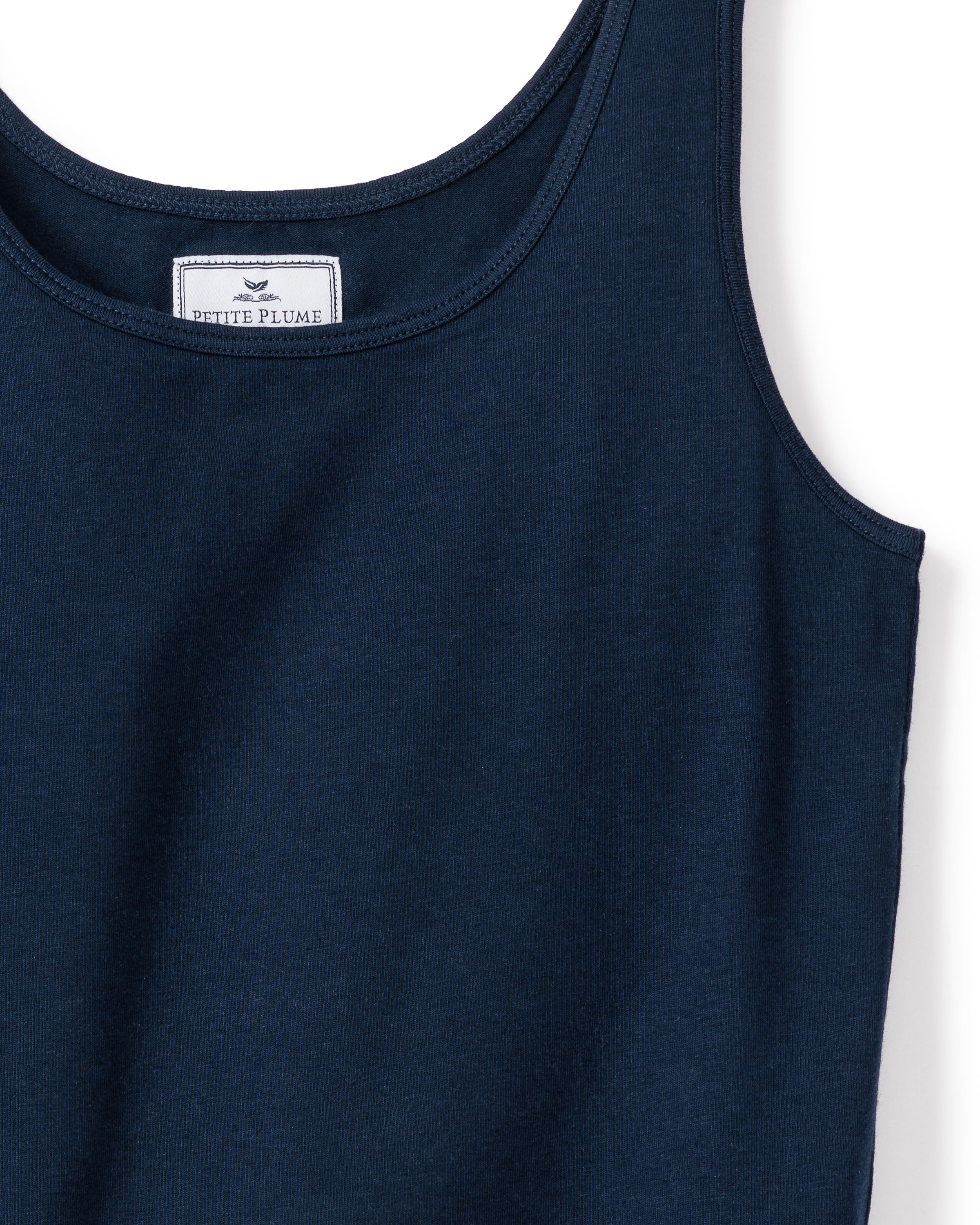 The Womens Pima Tank Top in Navy by Petite Plume is a close-up of stylish sleepwear, showcasing a round neckline. A white label with Petite Plume and a feather logo is visible inside. The fabric resembles soft, delicate jersey knit pajamas.