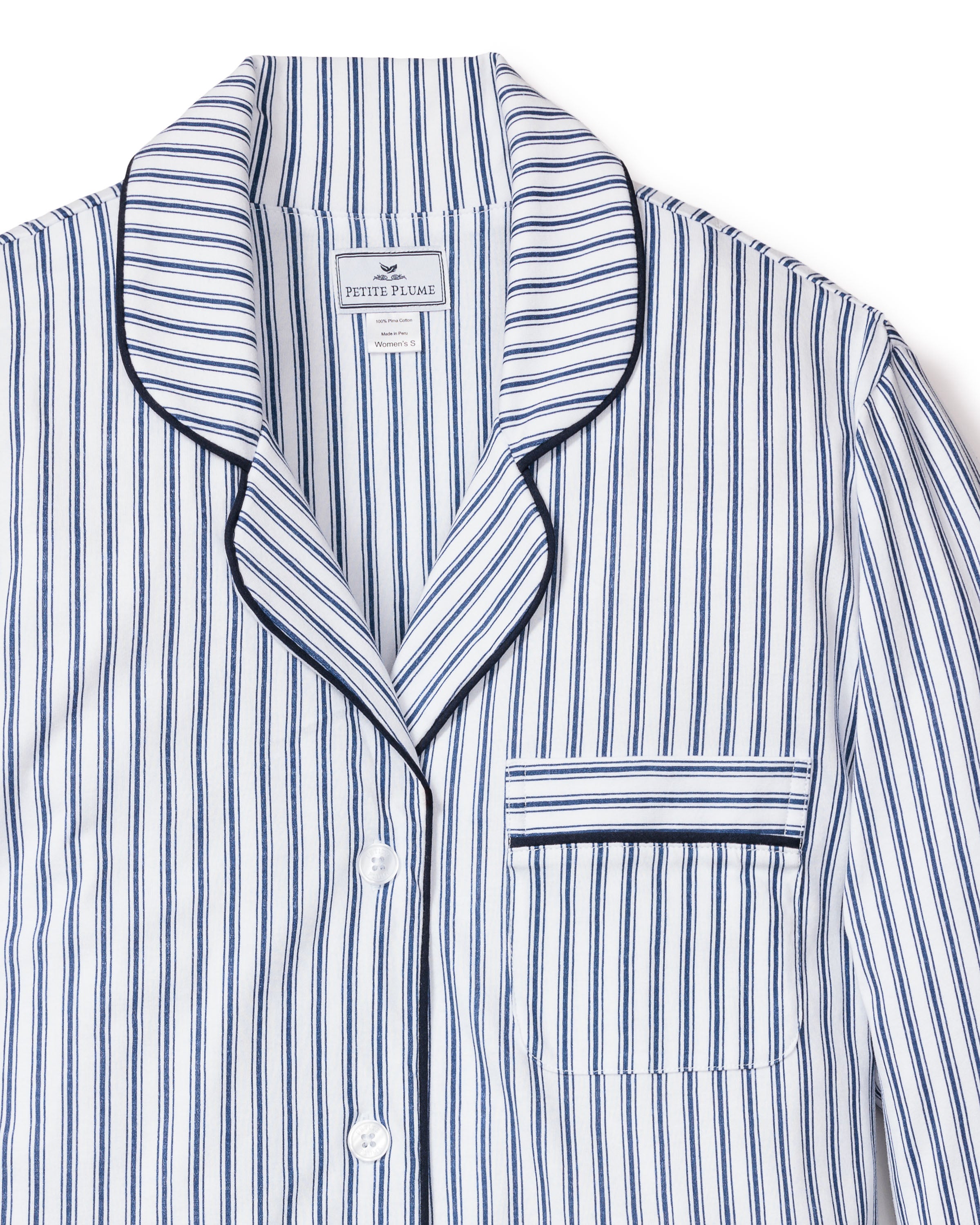 The Petite Plume Womens Pima Nightshirt in Navy French Ticking, crafted from luxurious Pima cotton, features a white and blue striped design with a collar, front pocket, black piping along the edges, and white buttons. The fabric label inside the collar highlights its premium quality.