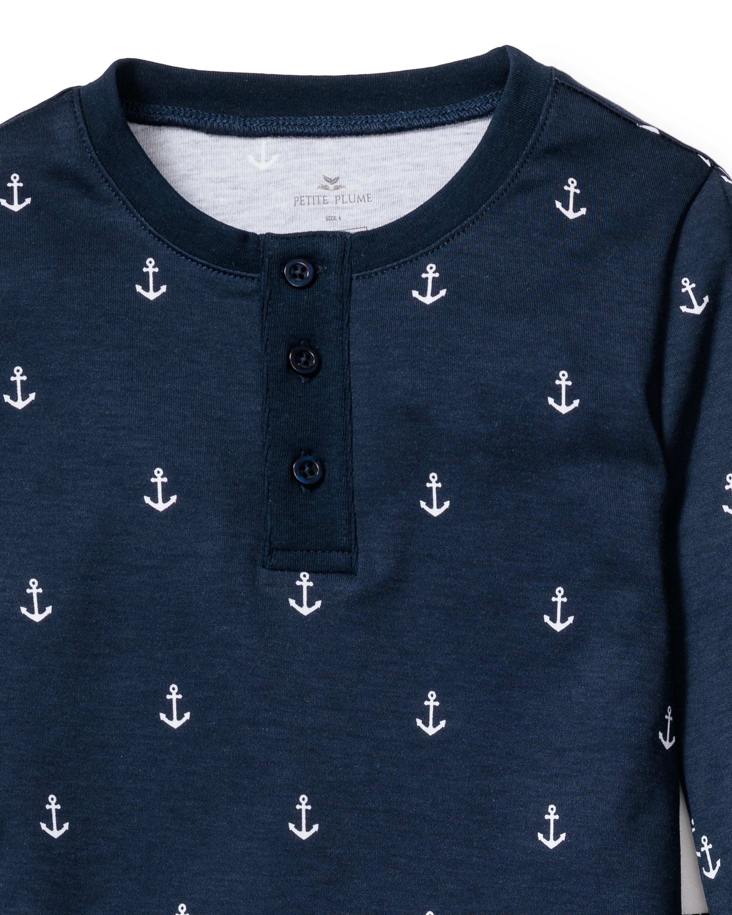 The Kids Pima Snug Fit Pajama Set in Portsmouth Anchors by Petite Plume features a navy blue top with a round neck and three-button placket, made from soft Pima Cotton with a pattern of small white anchors. Perfect for childrens sleepwear.