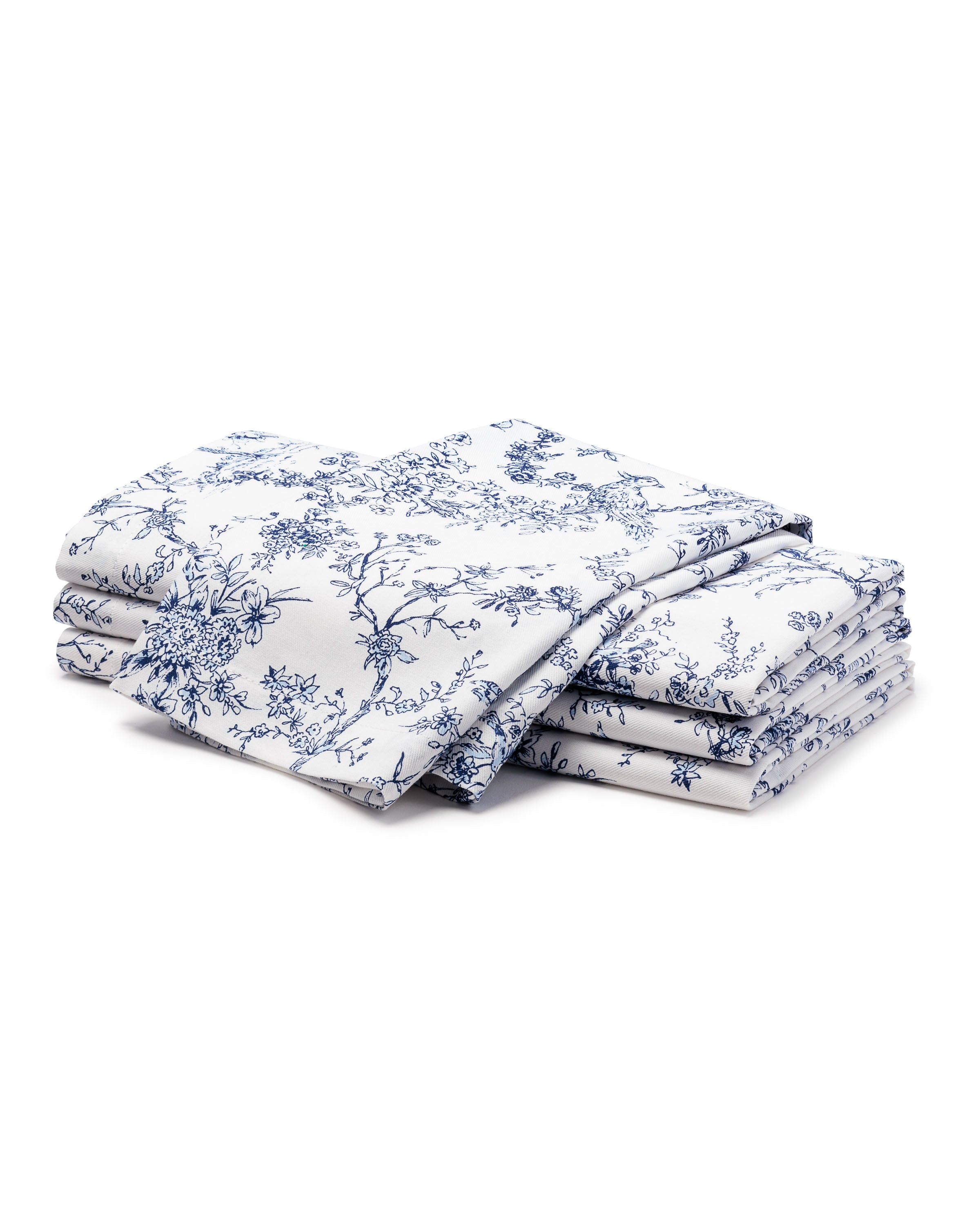 A stack of Signature Twill Napkins in Timeless Toile by Petite Plume, with a white backdrop and blue floral patterns, epitomizes elegance. The napkins are neatly arranged, showcasing intricate floral and branch designs reminiscent of delicate craftsmanship.