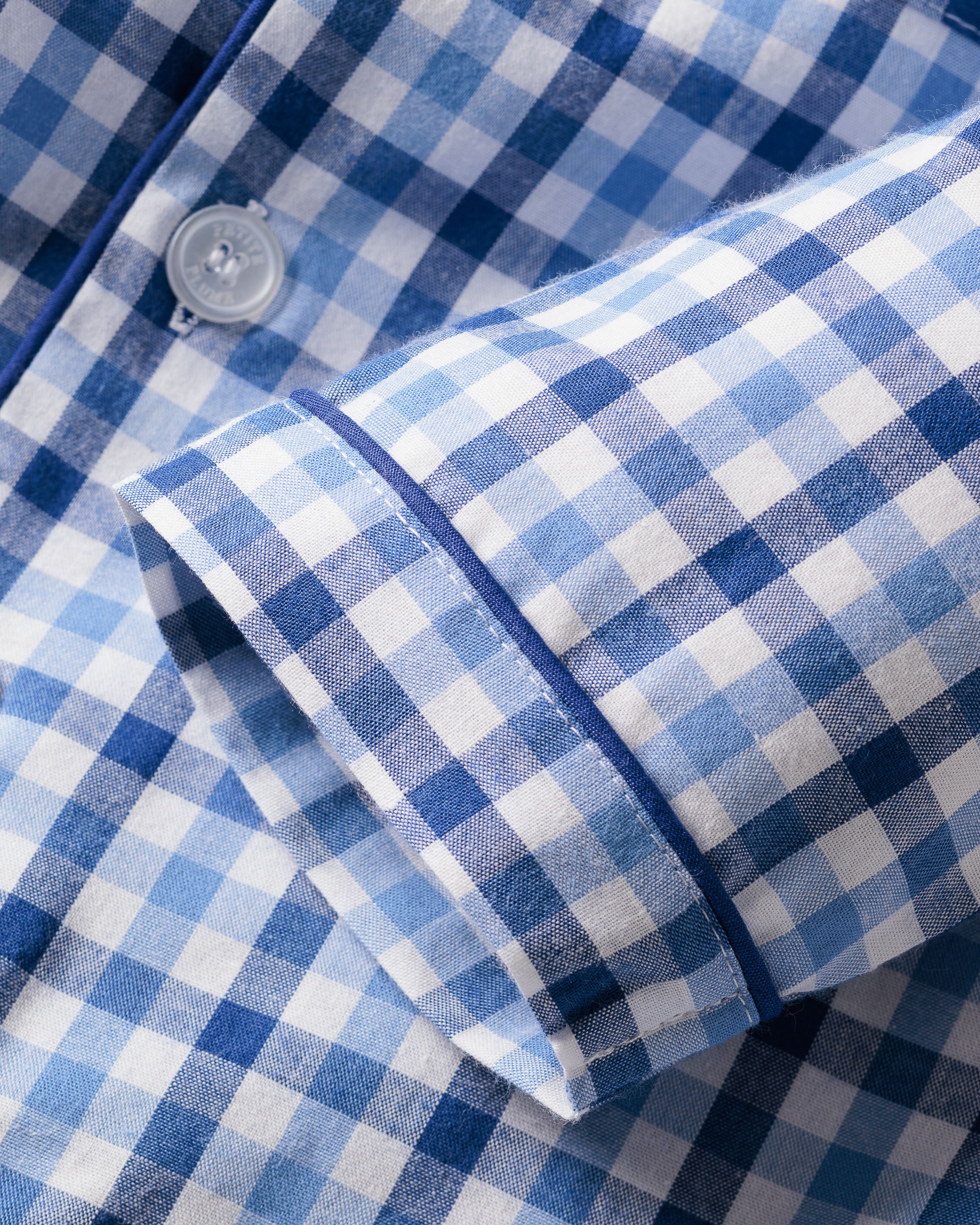 Close-up of Petite Plumes Kids Twill Pajama Set in Royal Blue Gingham, featuring a blue and white checkered sleeve with a white button and blue piping, reminiscent of classic pajamas.
