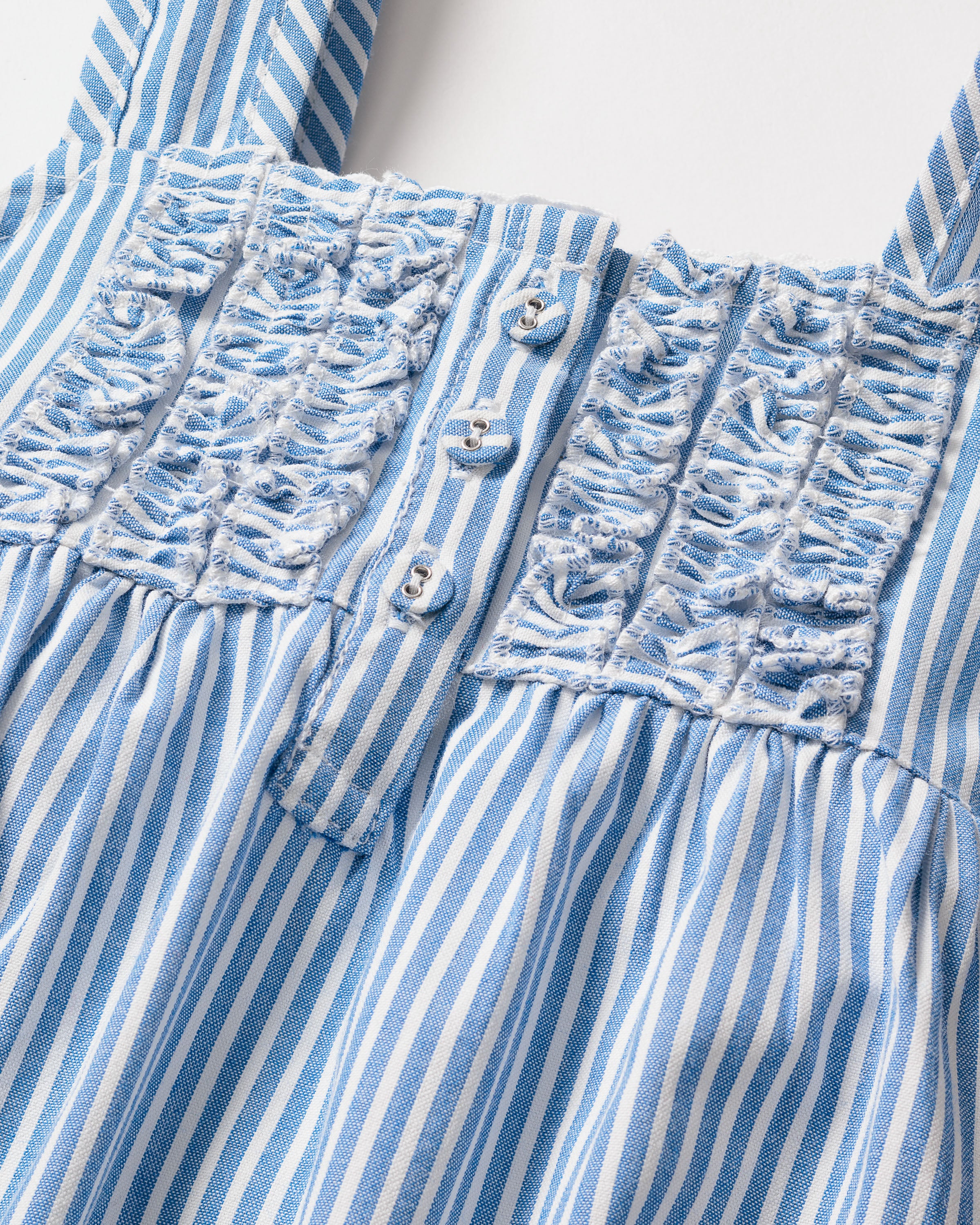 A close-up of Petite Plumes Girls Twill Charlotte Nightgown in French Blue Seersucker highlights the intricate smocked bodice detailing, with small buttons that enhance its delicate handcrafted look.