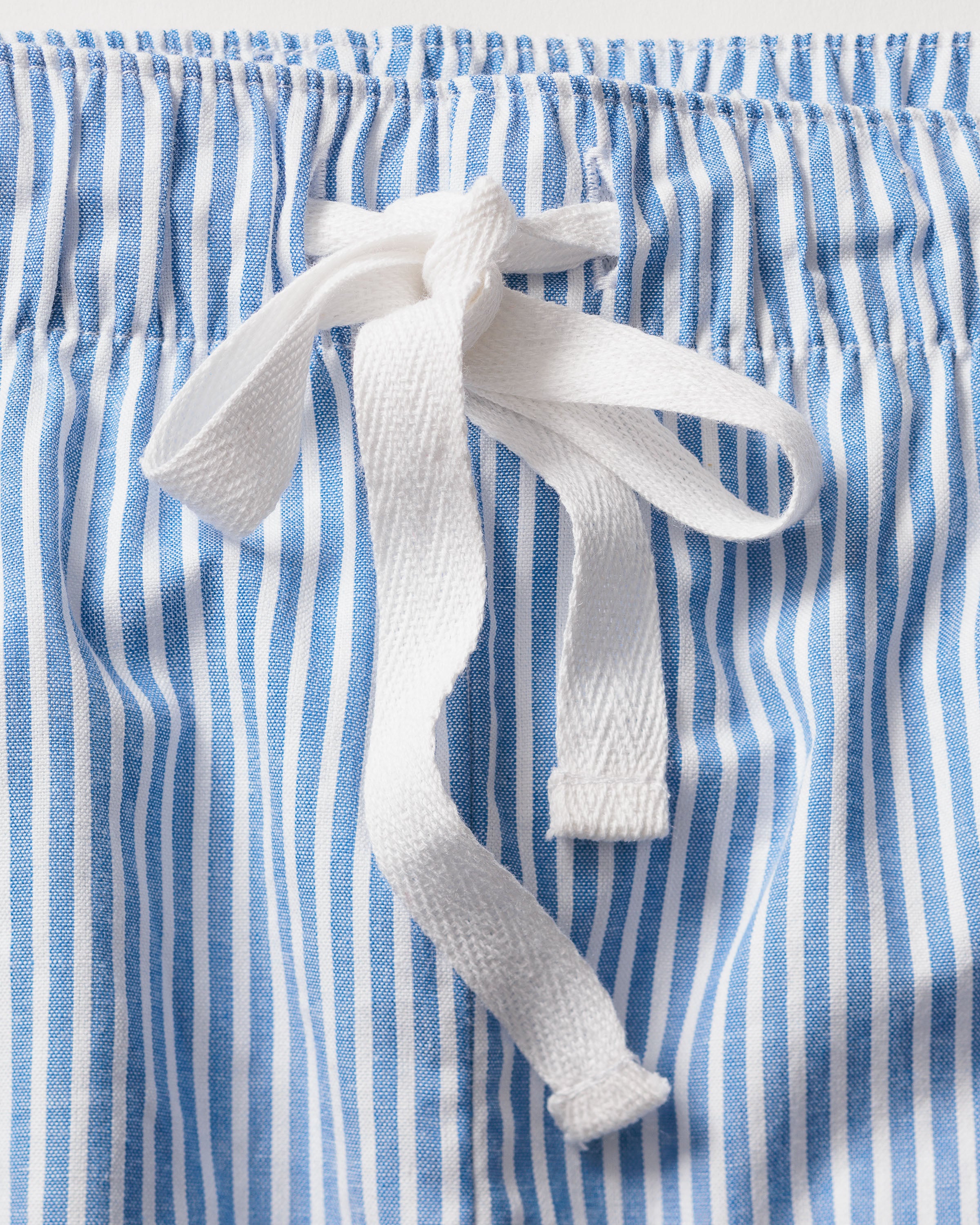 Close-up of Petite Plumes Womens Twill Pajama Set in French Blue Seersucker, highlighting the comfortable elastic waistband with a white drawstring bow at the center.
