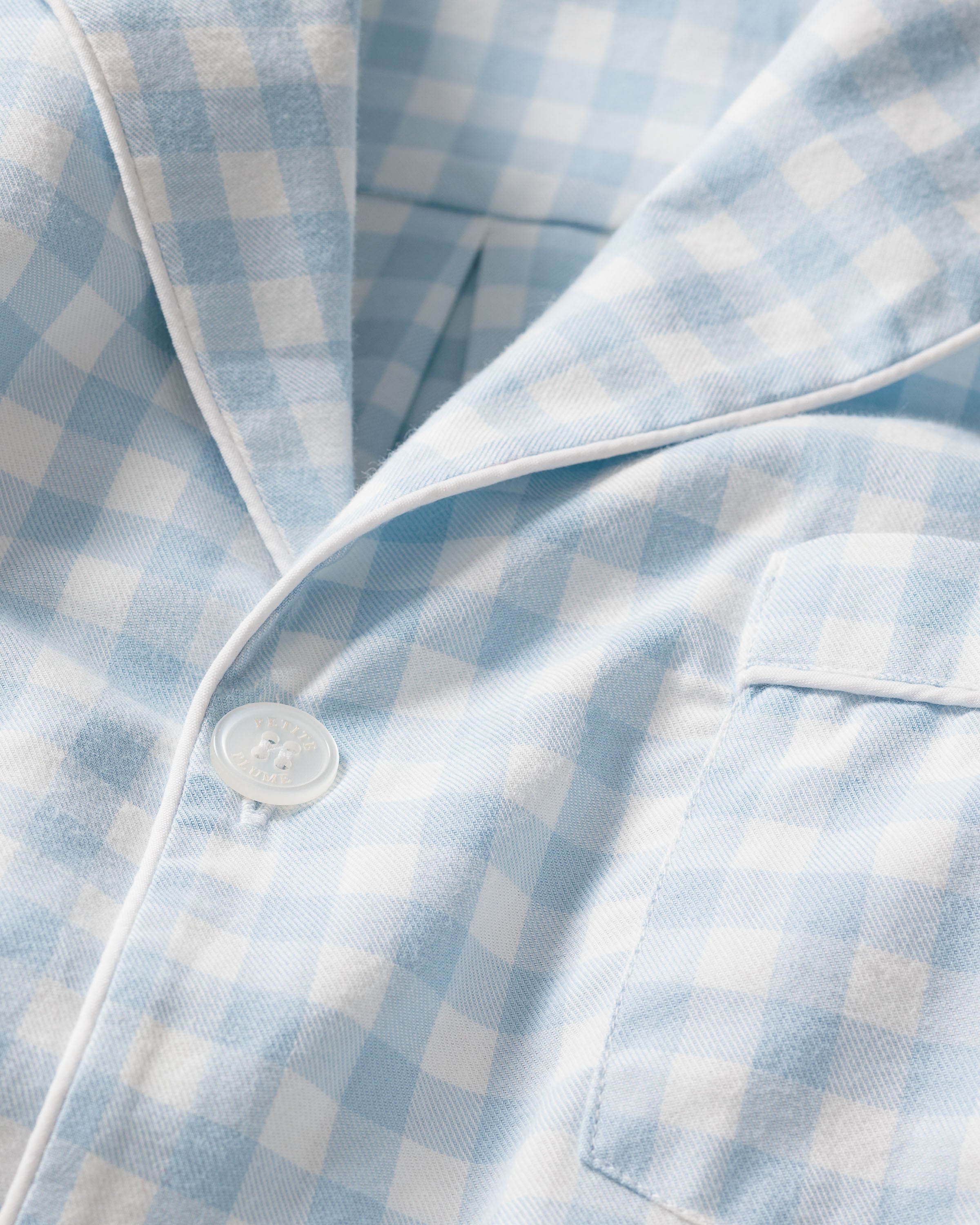 Close-up of Petite Plumes Mens Twill Pajama Set in Light Blue Gingham, showcasing a button and pocket. Crafted from the finest quality cotton, it offers a soft texture and classic pattern ideal for pajamas or casual wear.
