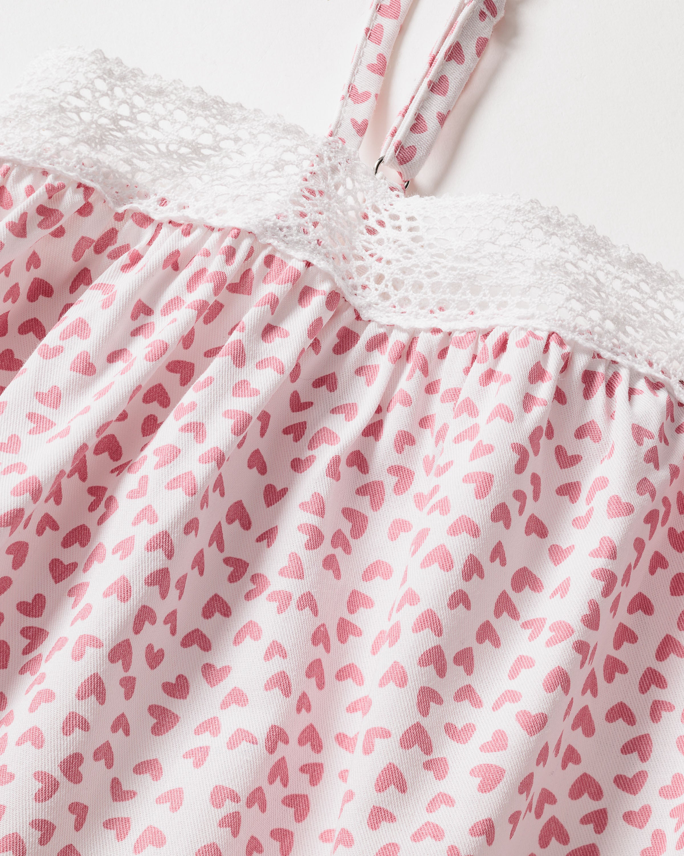 Close-up of Petite Plumes Girls Twill Lily Nightgown in Sweethearts, crafted from yarn-dyed cotton with pink hearts and a lace-trimmed top. Two thin straps accentuate its luxurious sleepwear design against a plain white background.