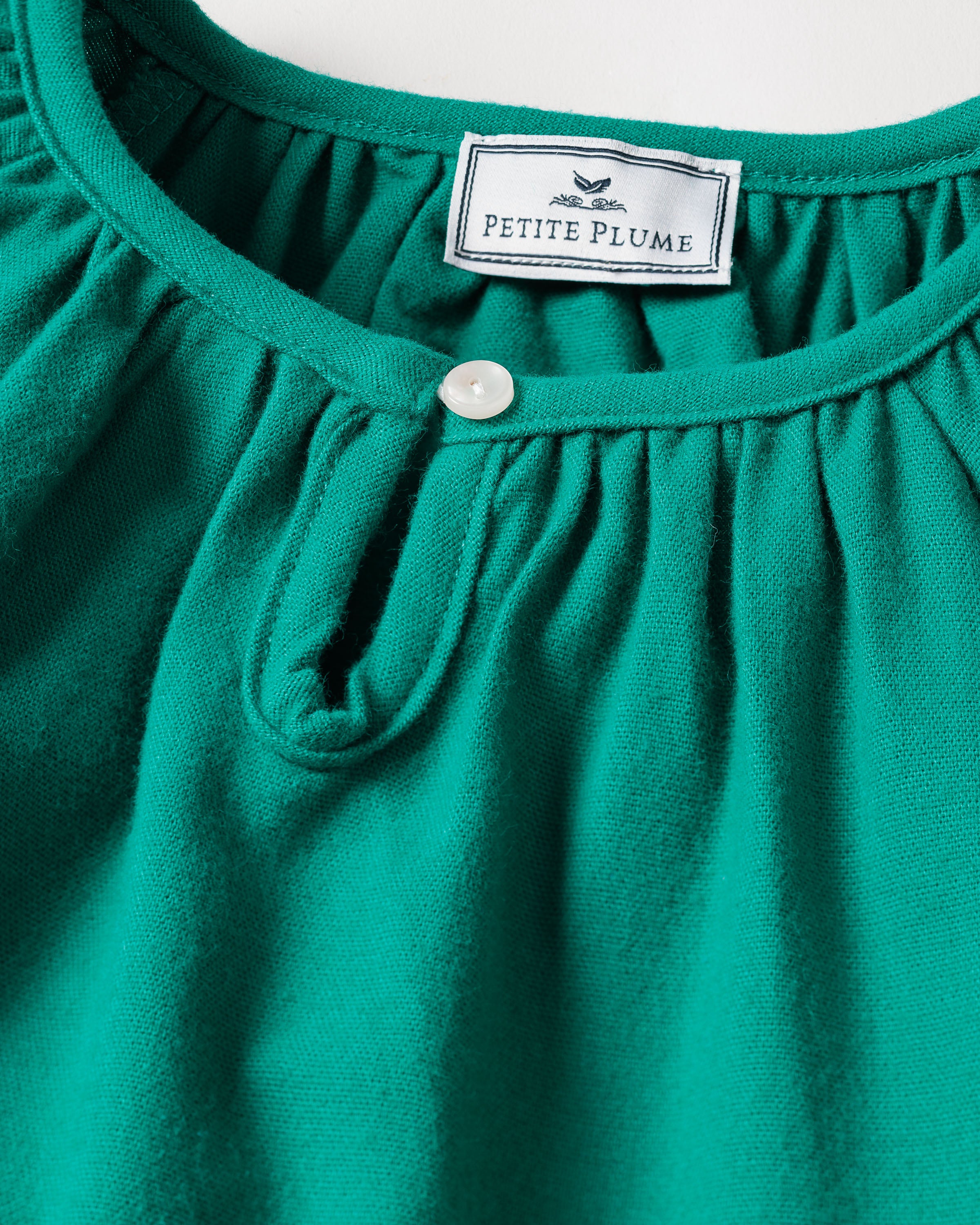 Close-up of the neckline on a green Girls Flannel Delphine Nightgown by Petite Plume, showcasing gathered fabric for a ruffled effect and featuring a round button.