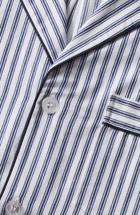 Close-up of a fabric with vertical navy blue and white stripes, featuring white buttons, a notched collar, and a small pocket with matching striped trim.