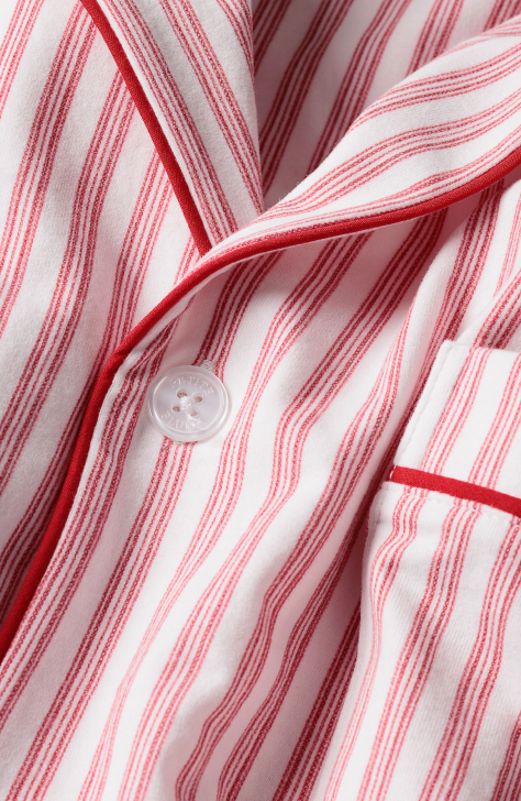 Close-up of a red and white striped fabric, likely a pajama top, showing a white button, collar, and a pocket with red piping detail.