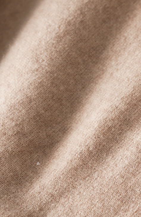 Close-up of beige, soft textured fabric with gentle folds and shadows, highlighting its smooth and cozy surface.