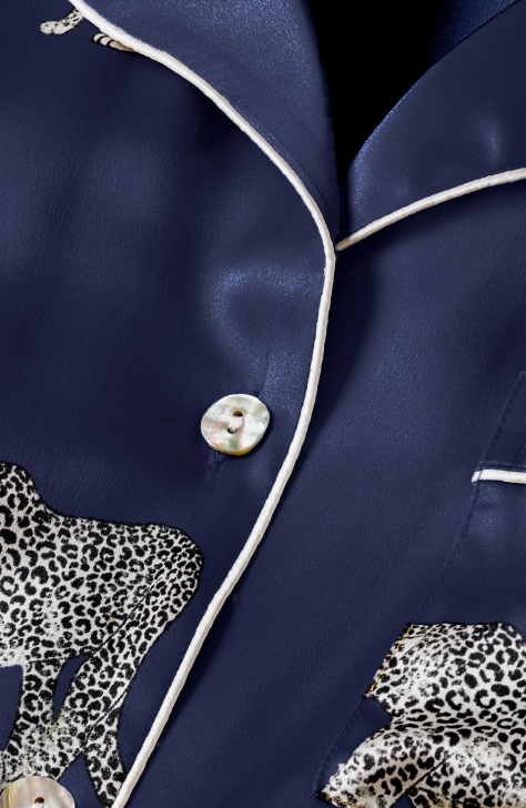 Close-up of a navy blue satin pajama top with white piping, mother-of-pearl buttons, and a printed pattern of leopards in black and white.