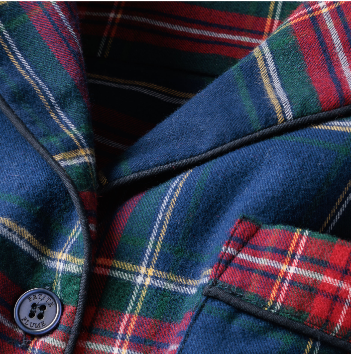 Close-up of a plaid fabric jacket in red, green, blue, and yellow with a dark blue button and a pocket. The fabric appears soft, with visible stitching and a classic tartan pattern.