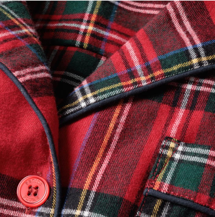 Close-up of a red, green, and yellow tartan plaid fabric with a dark piping edge, a red button, and a pocket flap visible, likely part of a tailored garment or jacket.