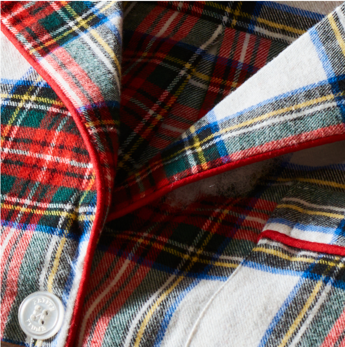 Close-up of a colorful plaid flannel fabric with intersecting red, green, blue, and yellow stripes, white background, red piping along the edge, and a white button visible in the lower left corner.