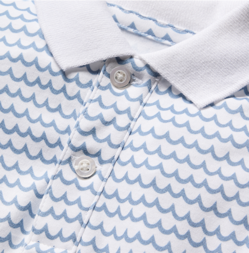 Close-up of a white polo shirt featuring a blue wave-like pattern and a white collar, with three white buttons on the front placket.