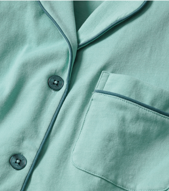 Close-up of a light green pajama shirt with navy piping, two buttons, and a breast pocket. The fabric appears soft and comfortable.