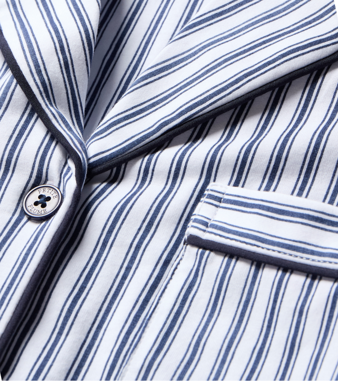 Close-up of a white fabric blazer with dark blue vertical stripes, a button, and a small front pocket with dark edging.