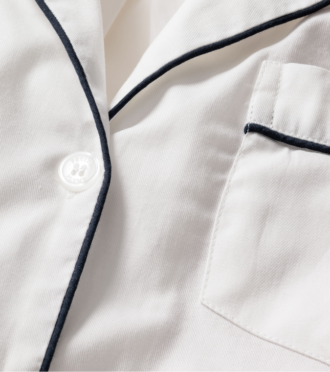 Close-up of a white pajama top with black piping along the collar, pocket, and edge, and a white button on the front.