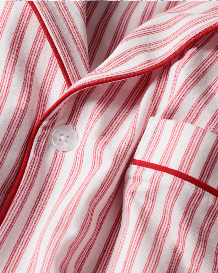 Close-up of a pink and white striped pajama top with red piping detail, a white button, and a pocket visible.