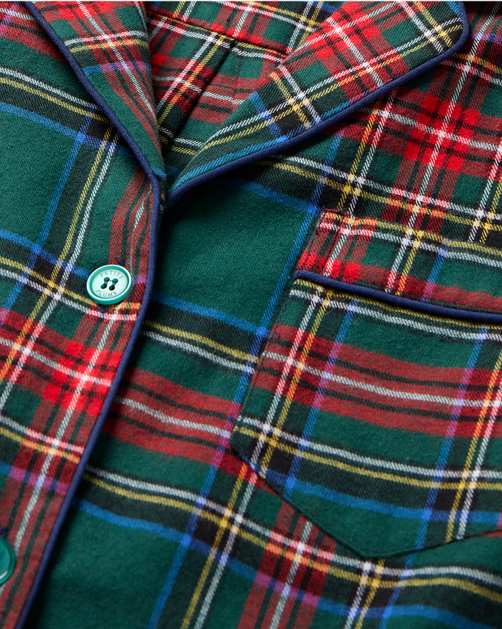 Close-up of a red, green, blue, and yellow plaid fabric with buttons and a pocket, likely part of a shirt or jacket. The fabric has a classic tartan pattern and a soft, woven texture.