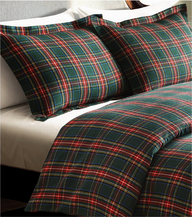Two pillows and a comforter with a green, red, yellow, and white plaid pattern are arranged on a neatly made bed with white sheets.