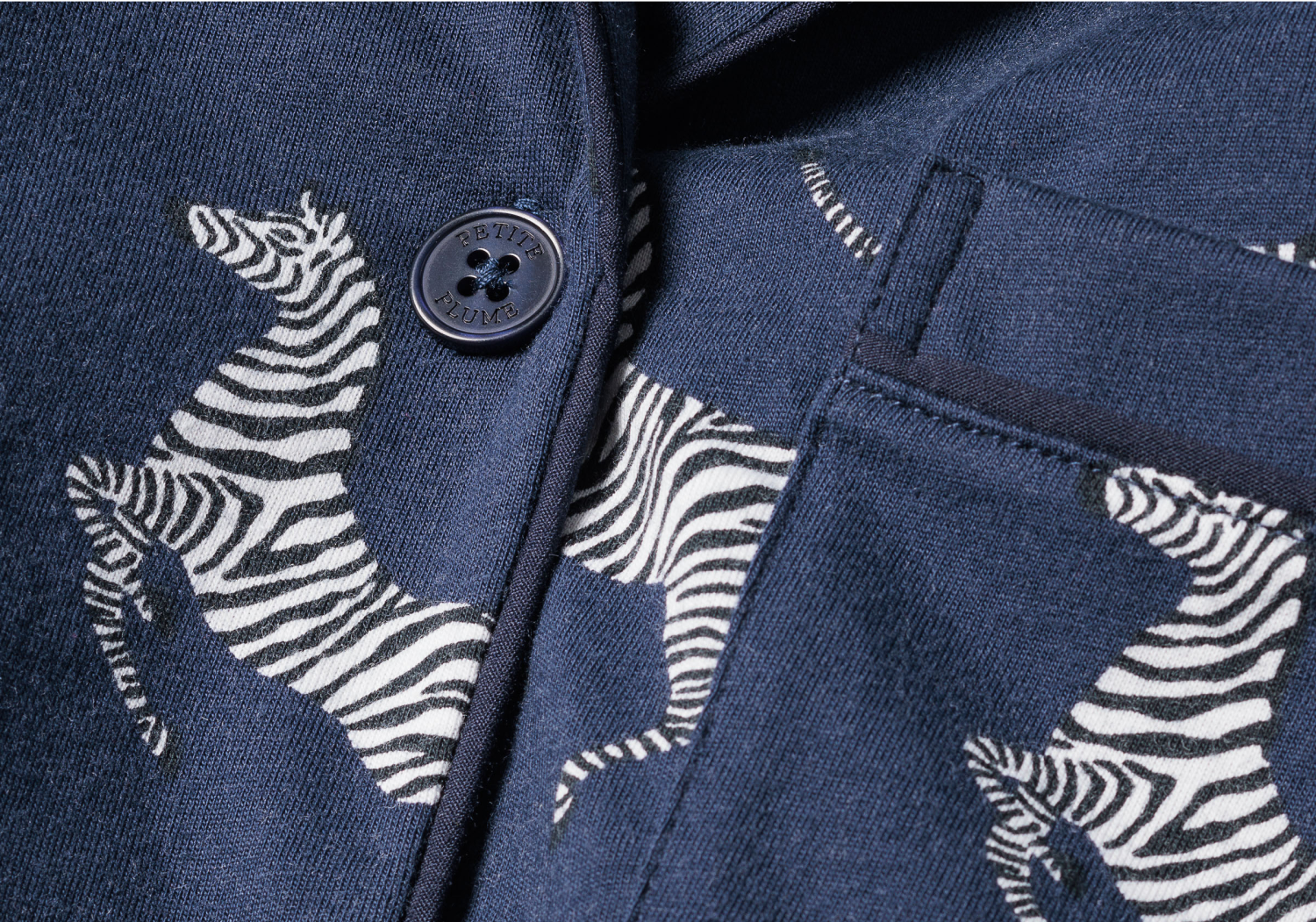 Close-up of a navy blue fabric with white zebra patterns, a dark blue button, and part of a front pocket visible.