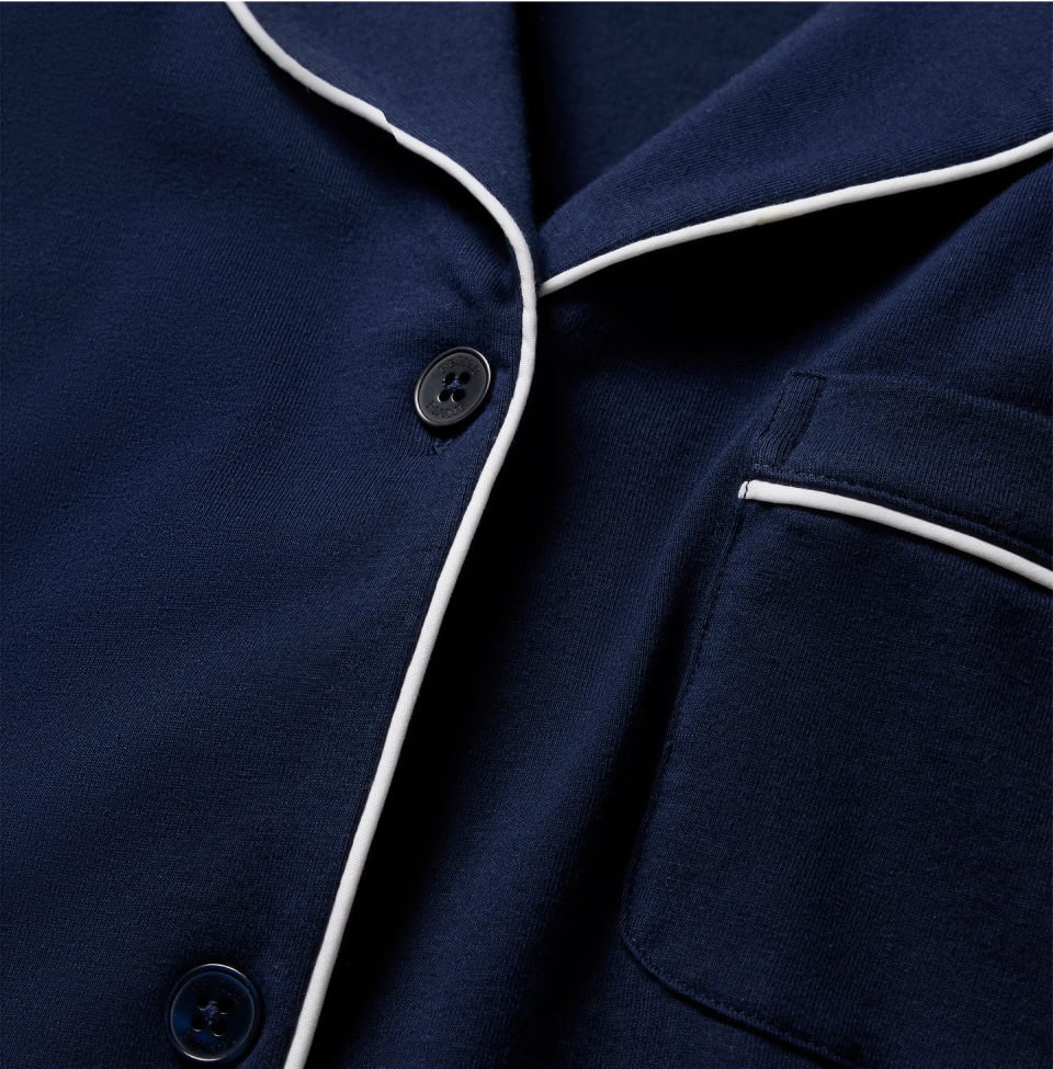 Close-up of a navy blue pajama top with white piping along the collar and pocket edges, and two dark buttons visible on the front.