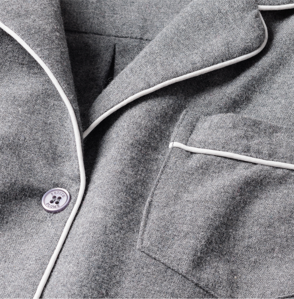 Close-up of a gray pajama top with white piping along the collar, pocket, and front edge. A single button with the word “Equate” is visible near the bottom left corner.