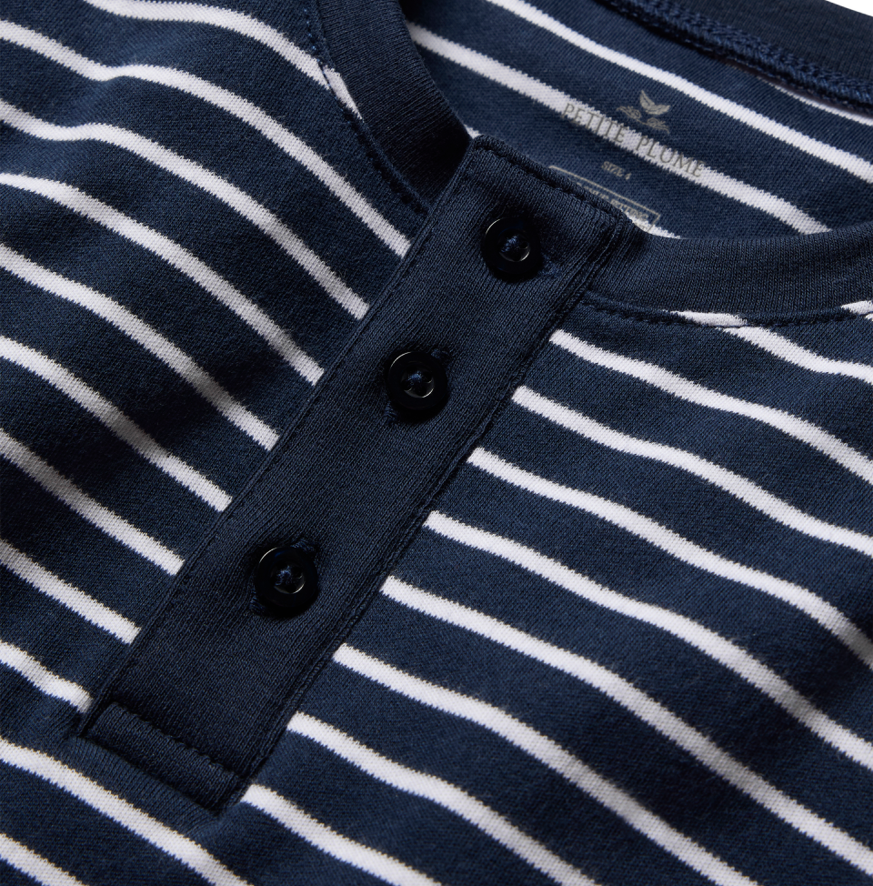 Close-up of a navy blue and white striped shirt with a round neckline and three black buttons on a placket down the front. The fabric label inside the collar is partially visible.